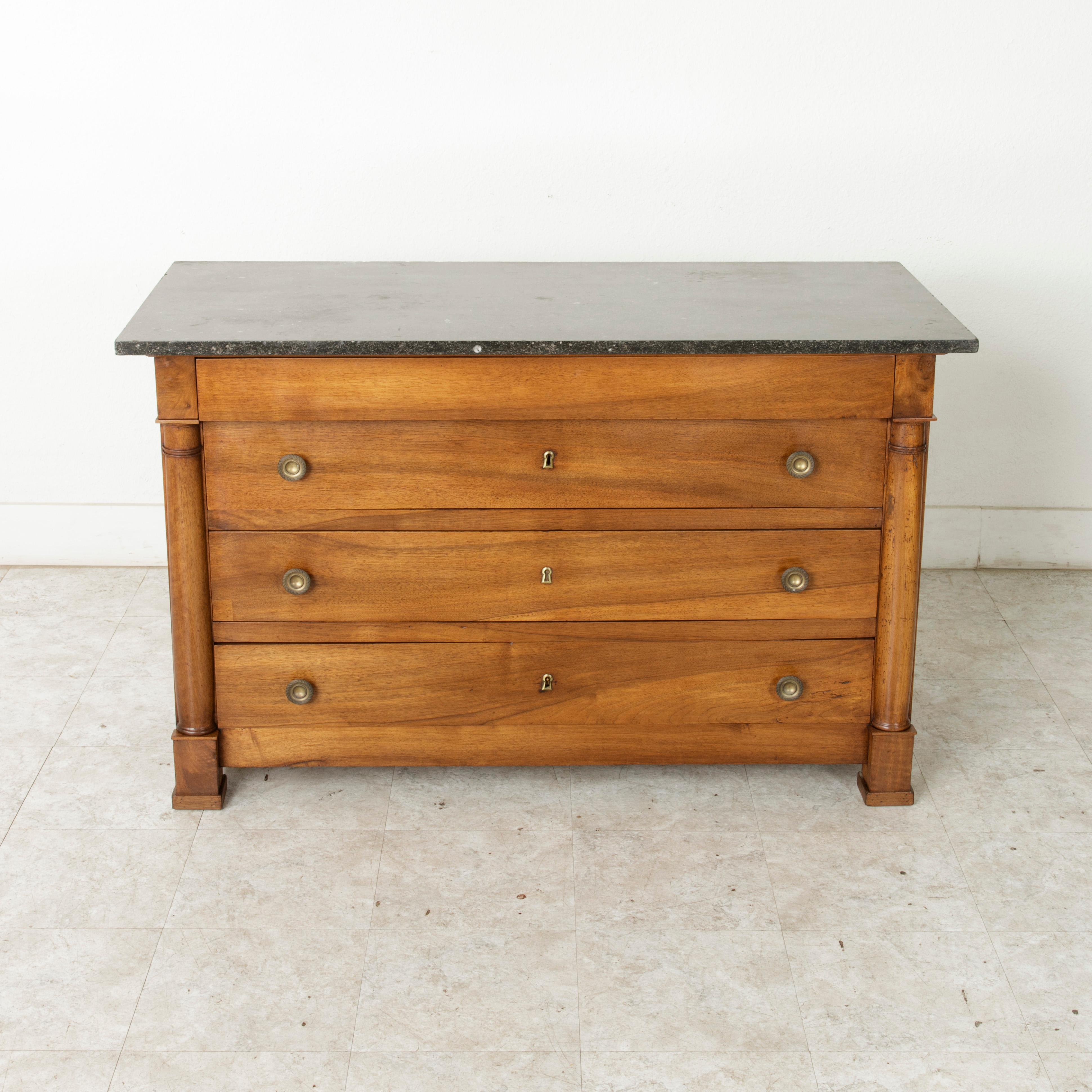 This late 19th century French Empire style walnut commode or chest features a solid black marble top. Its panelled sides are hand pegged and two classic half columns flank the front of the piece. Three drawers of dovetail construction are fitted