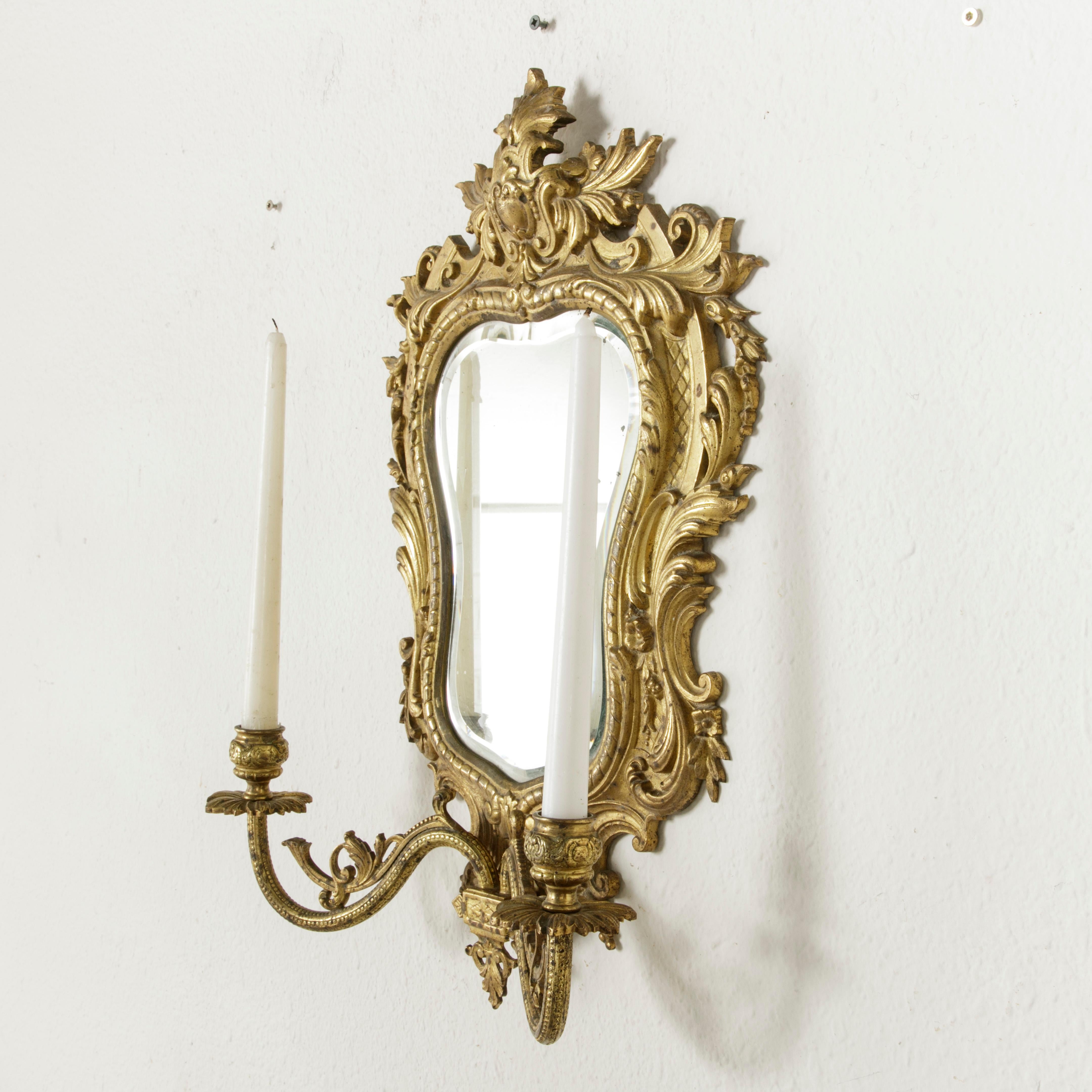 This late 19th century French gilt bronze girandole or wall mirror sconce features a beveled mirror and two candleholders. A beautifully executed decorative object, its original function was to increase illumination by reflecting the light from the