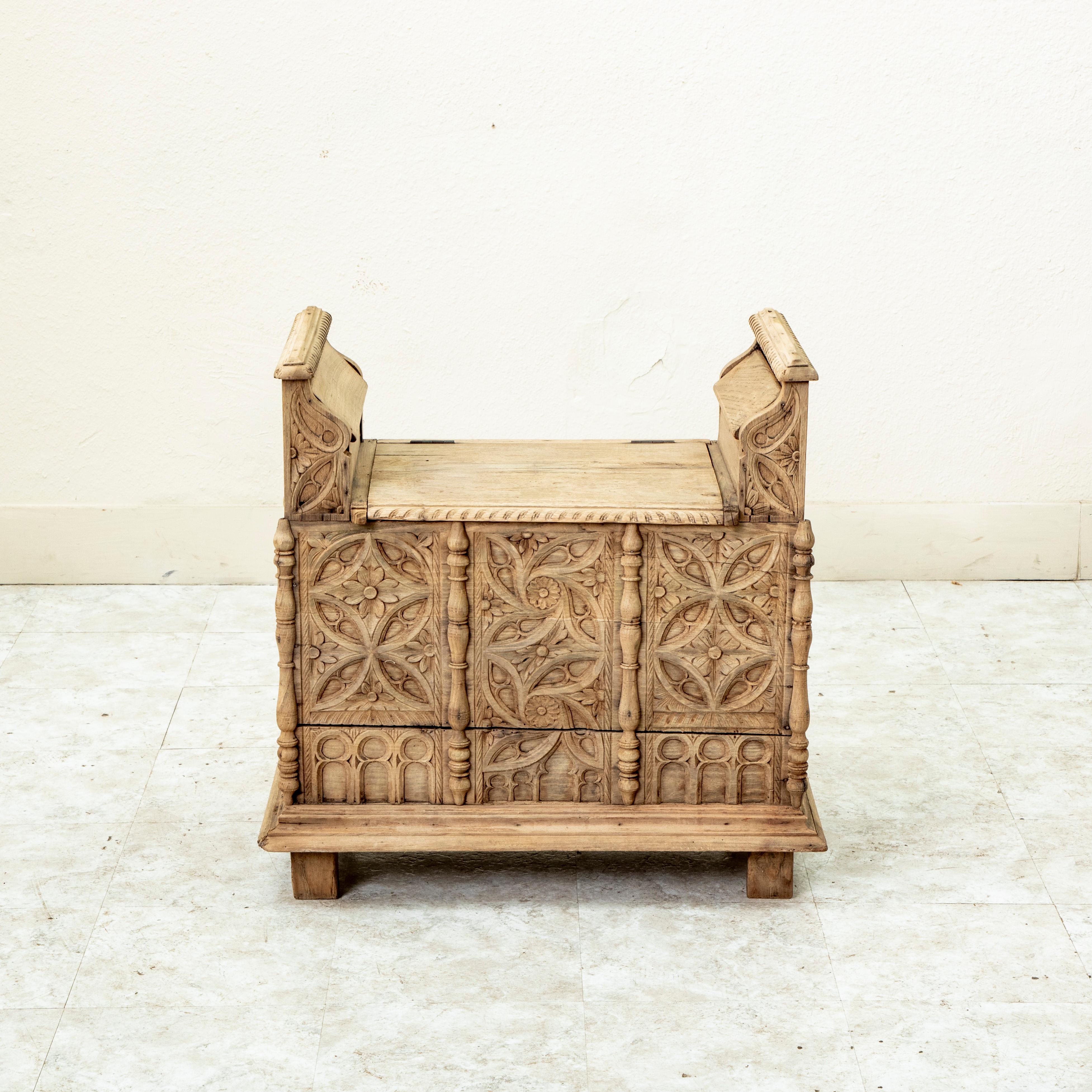 This small scale late nineteenth century French Gothic style coffer bench is constructed of solid hand carved bleached oak. Three hand carved panels on the front are detailed with a rosette pattern with geometric curves above and a gallery of arches