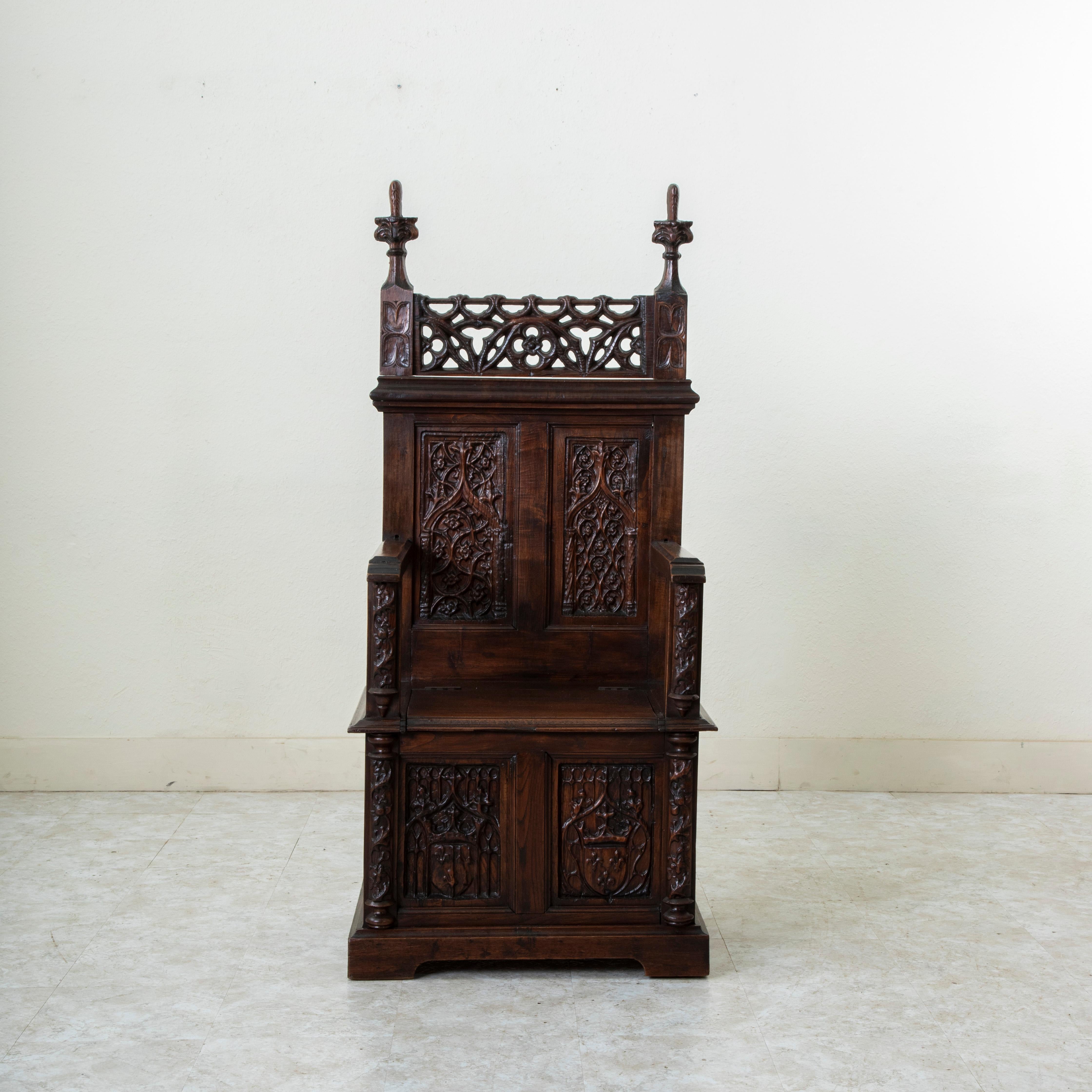 This late nineteenth century French Gothic style oak coffer armchair features eight hand carved panels in the lower apron and seat back, each with different Gothic motifs. The two lower panels of the seat are additionally detailed with coats of arms