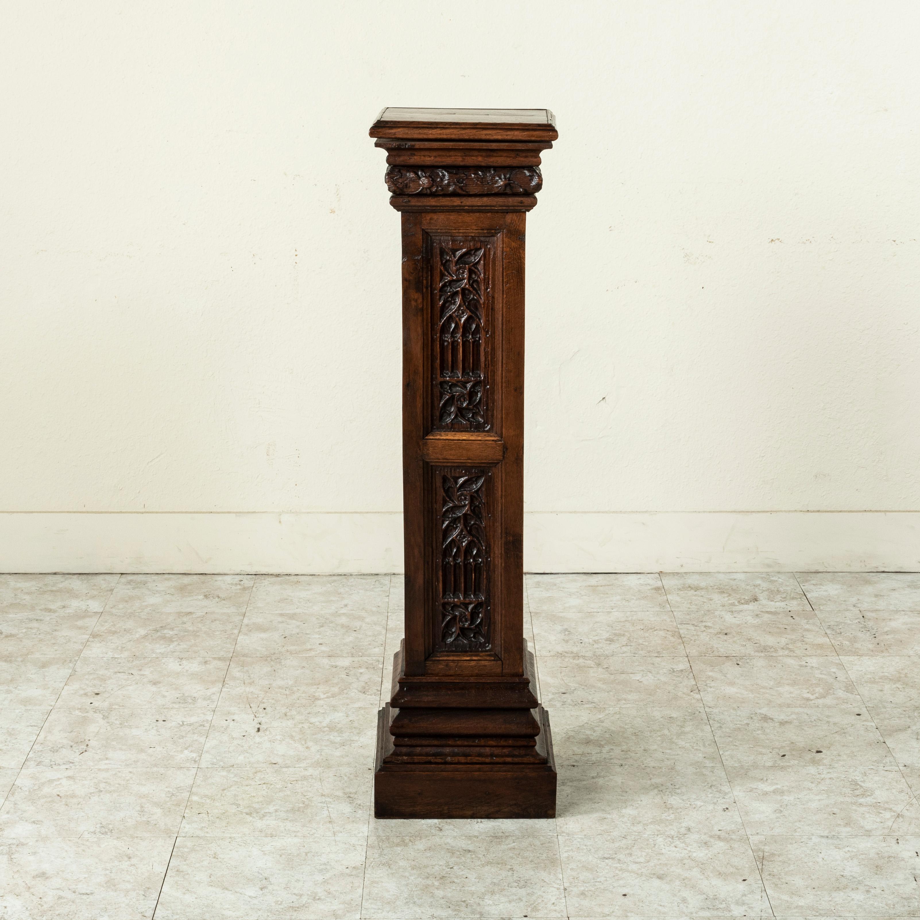 This late 19th century French Gothic style column, pedestal, or plant stand is constructed of solid oak. Hand carved panels on all four sides feature Classic Gothic arches and pinwheels. Below the square top are carved details of leaves and flowers.