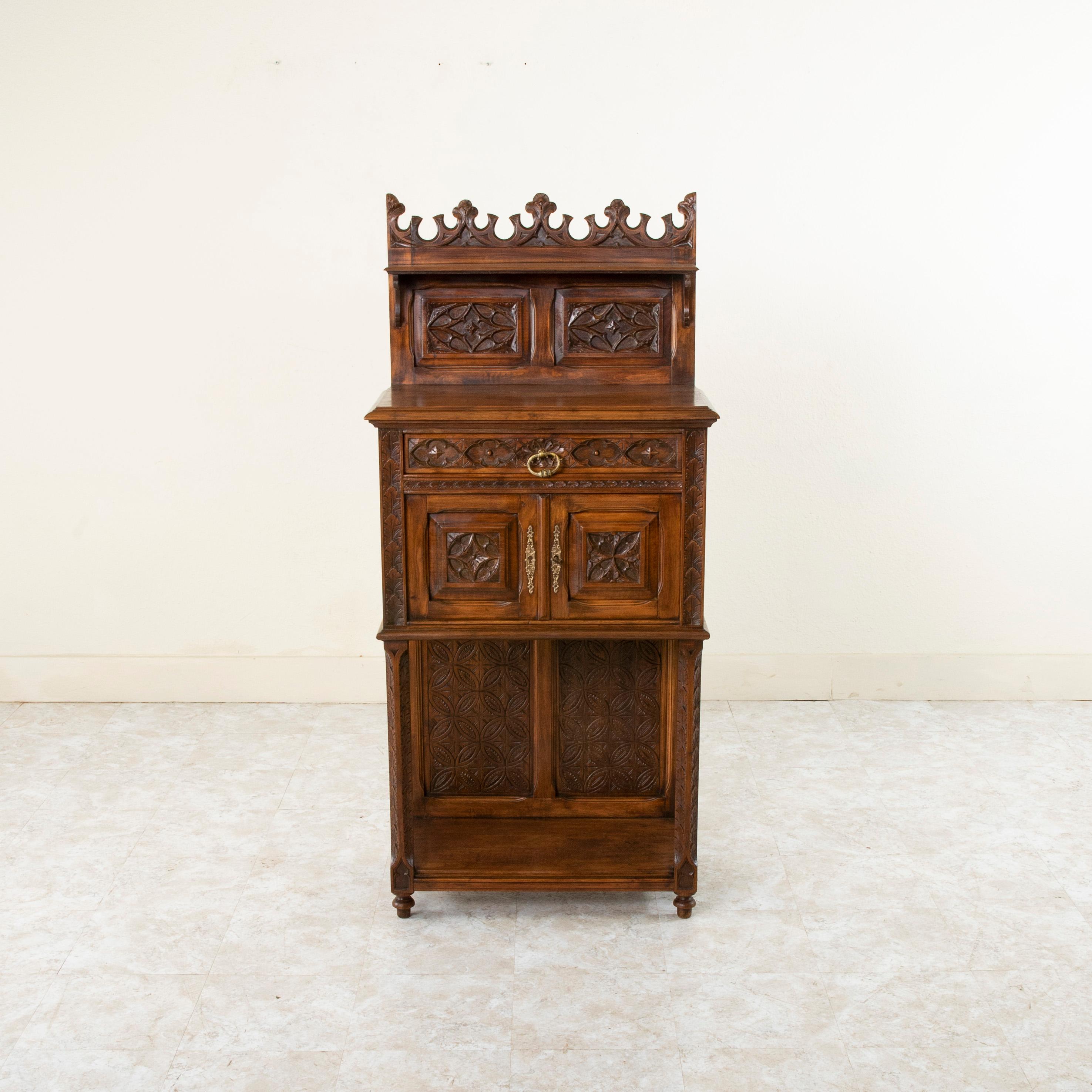 This late nineteenth century French Gothic style cabinet is constructed of solid walnut and features hand carved detailing of Gothic motifs on all of its forward facing panels, doors, and drawer. The single drawer of dovetail construction rests