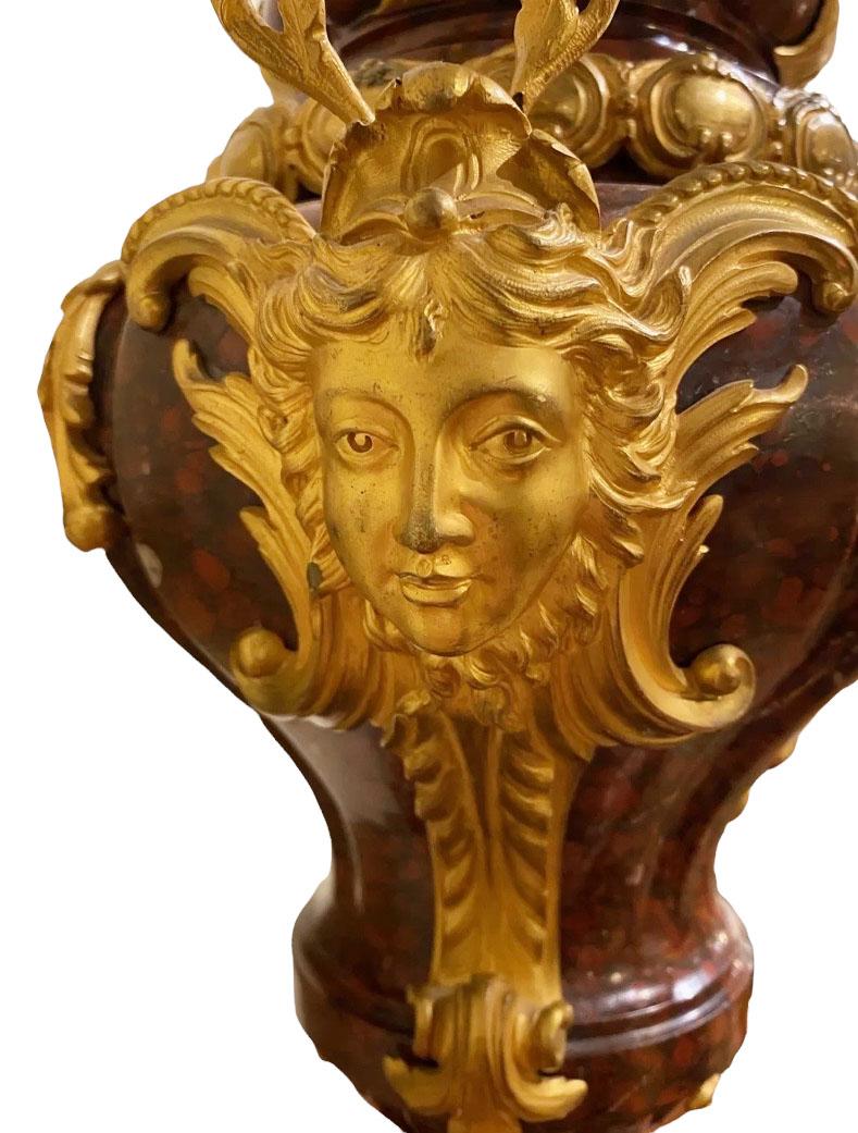 A fine pair of French ormolu bronze-mounted rouge Griotte marble urns with bronze mask handles, leaves with a flame finial top.