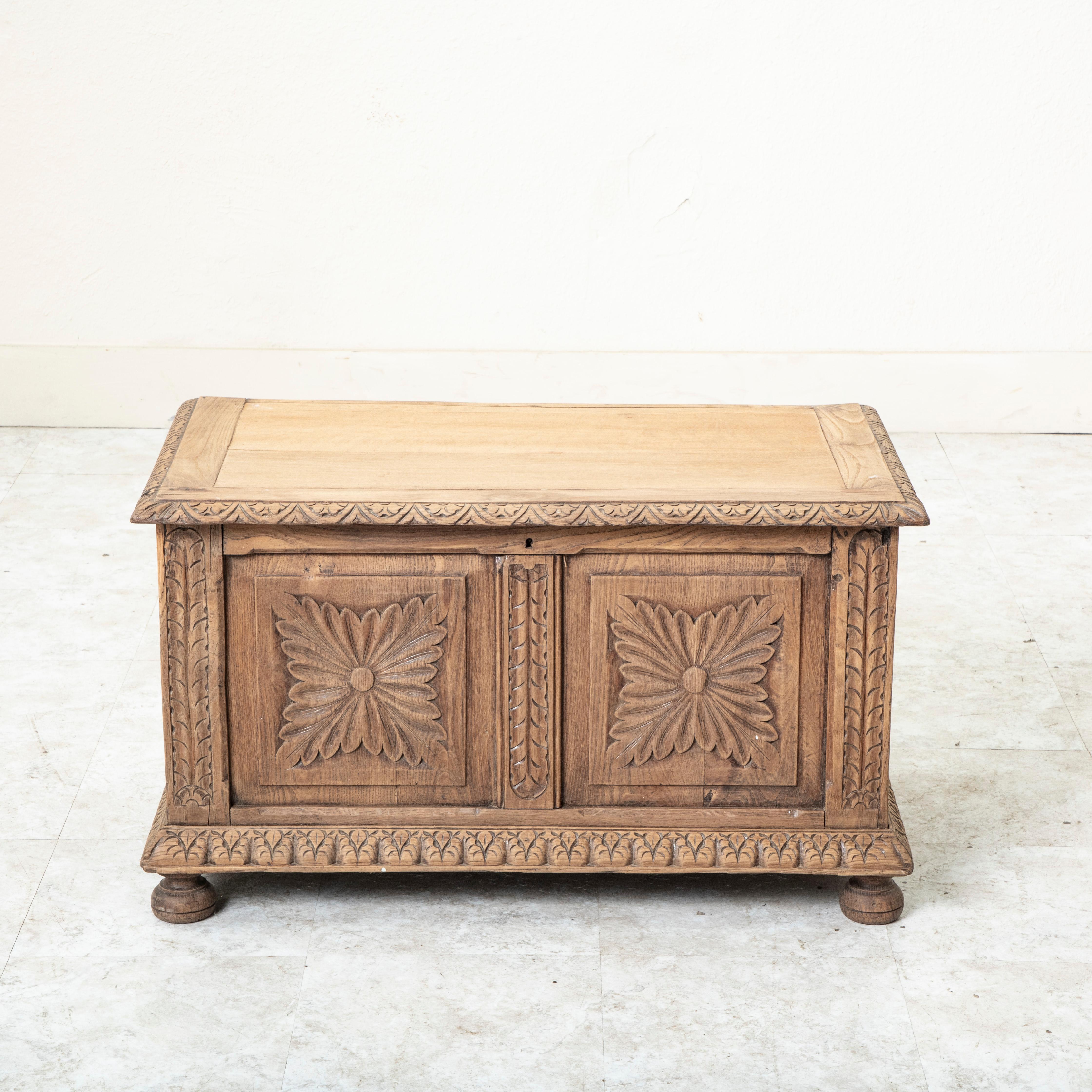 This late nineteenth century French hand carved oak coffer features four large panels, each with a large carved rosette in the center. The corners and lower apron are detailed with stylized leaves. Its hinged top has a beveled edge finished with an