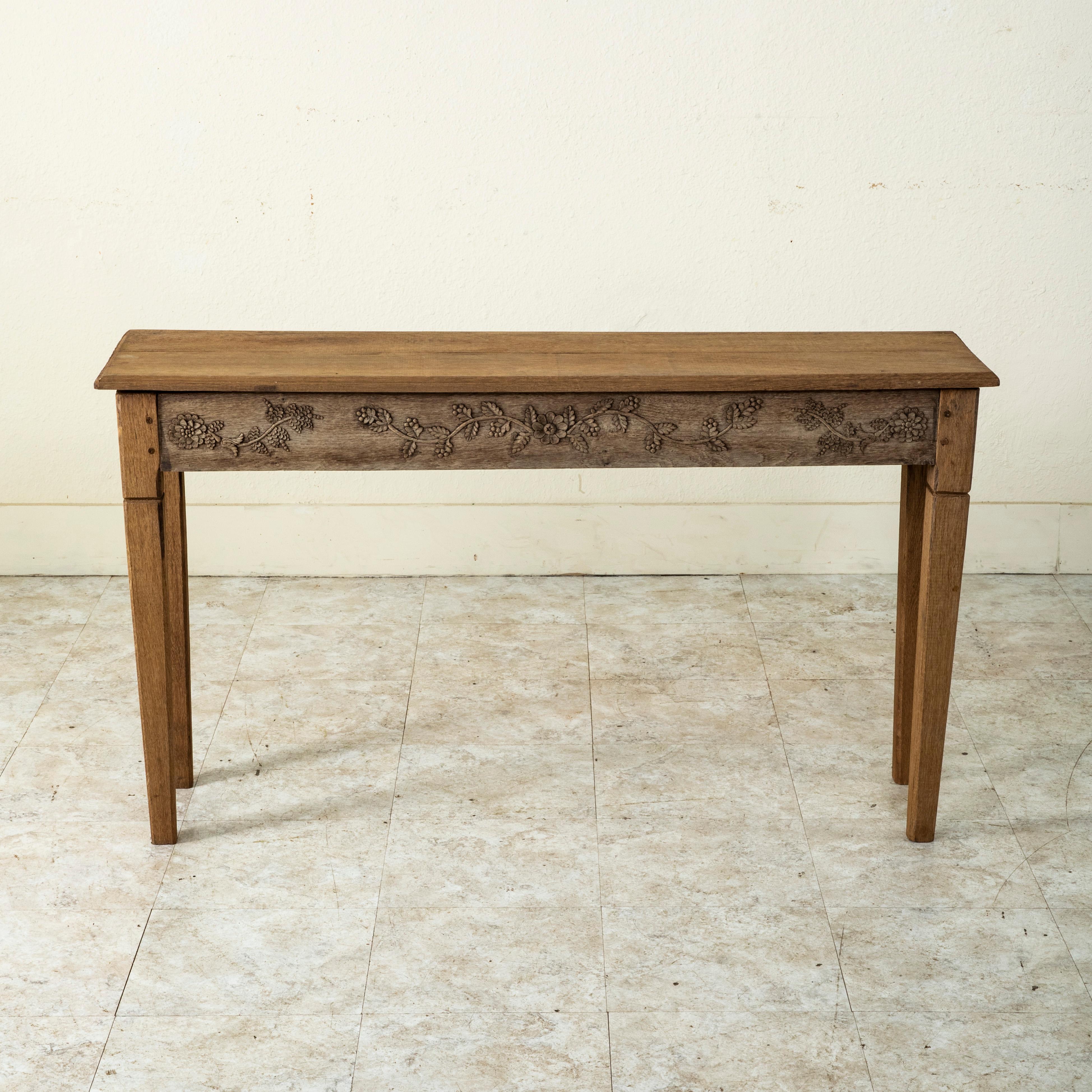 This late nineteenth century French bleached oak console table or sofa table features a hand carved frieze of flowers on the facade. The beveled top rests on a hand pegged base with tapered square legs. c. 1890.   