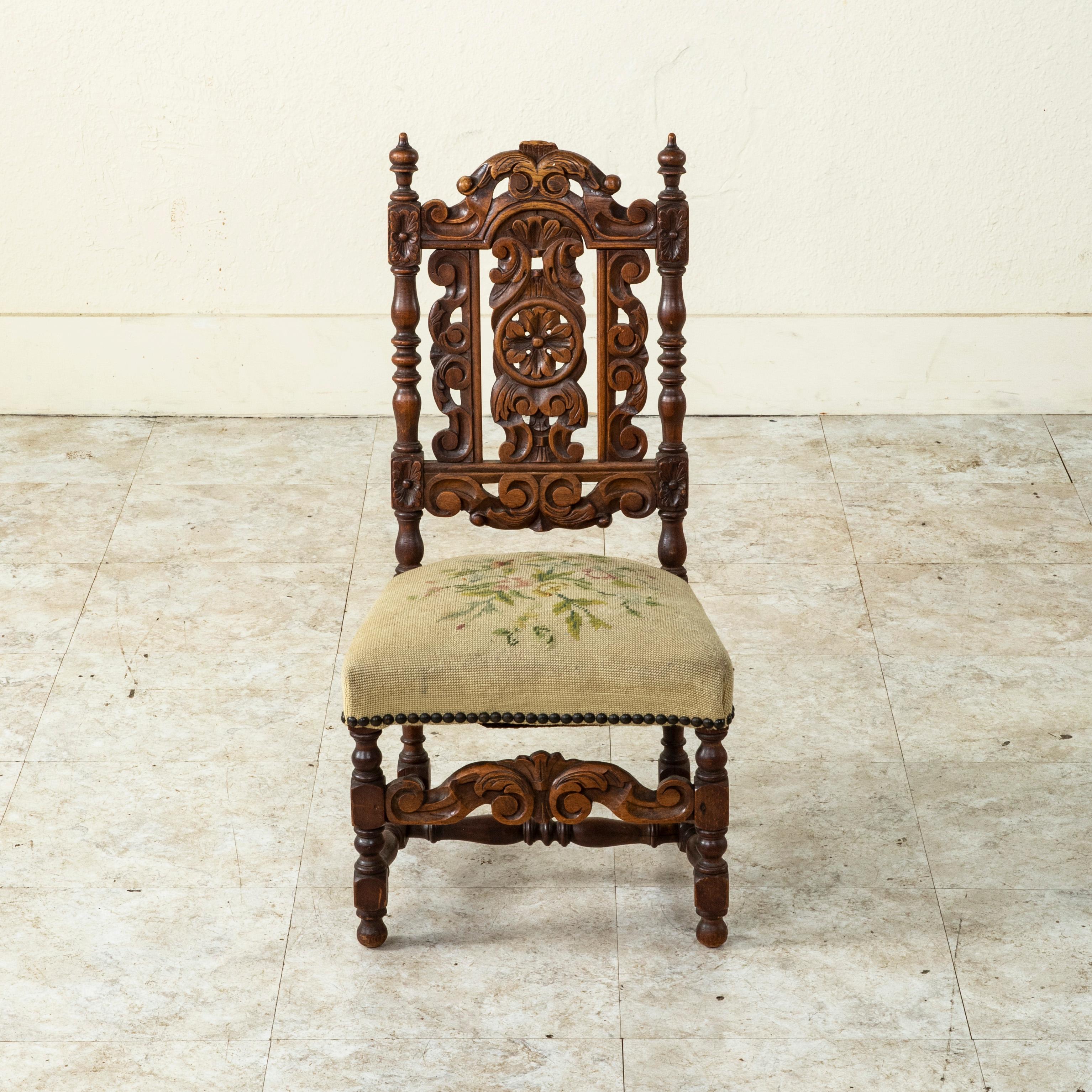 This late 19th century French oak child's chair features a seat back with hand carved rosettes at the corners, scrolling leaves, a central rosette, and finials. The seat rests on turned legs joined by a turned H-stretcher. A hand carved panel joins