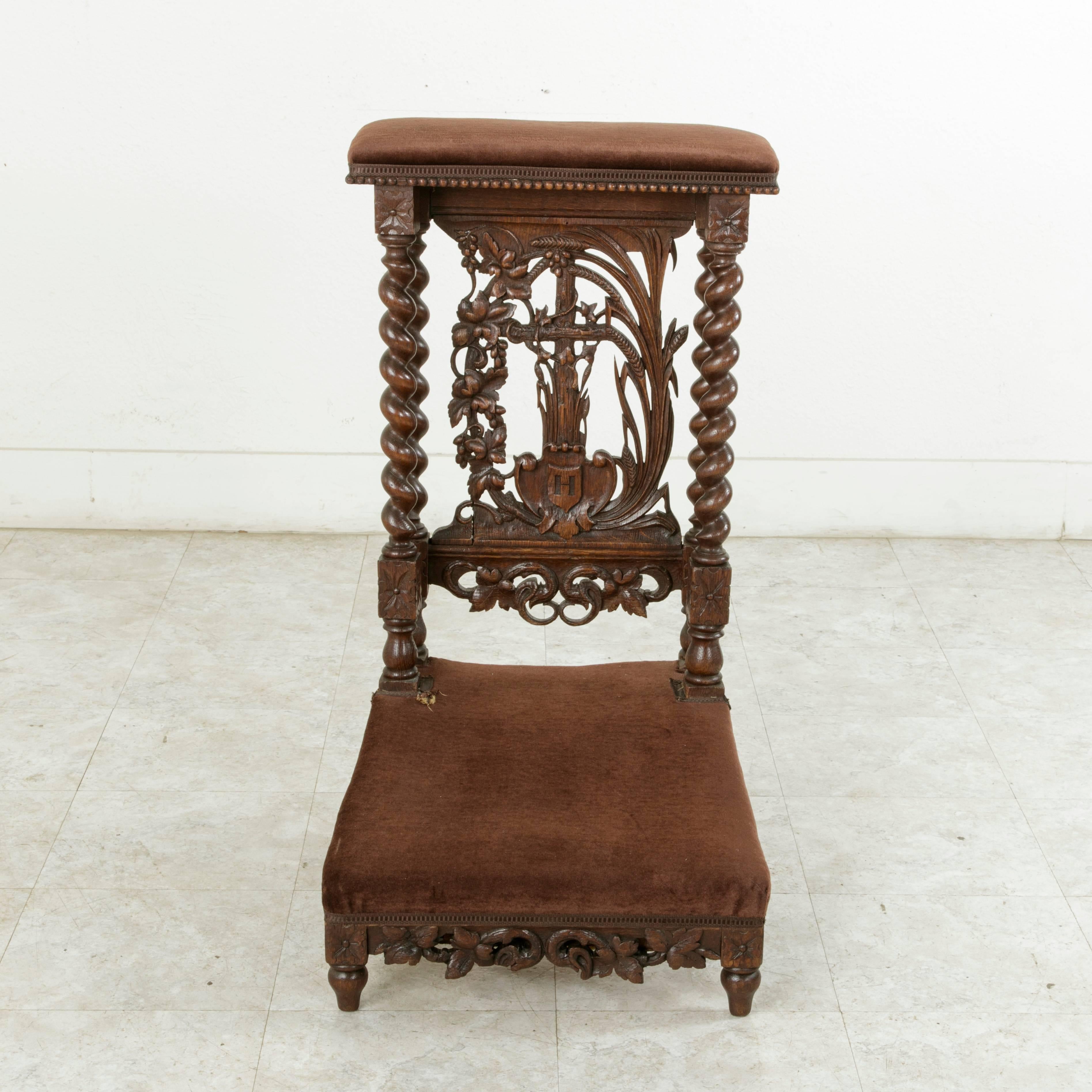 This French hand-carved oak prayer chair, or prie-dieu, in French, features double barley twist columns at the back that support the armrest. Rosettes adorn the die joints at the top and bottom of the columns. The back displays an intricately