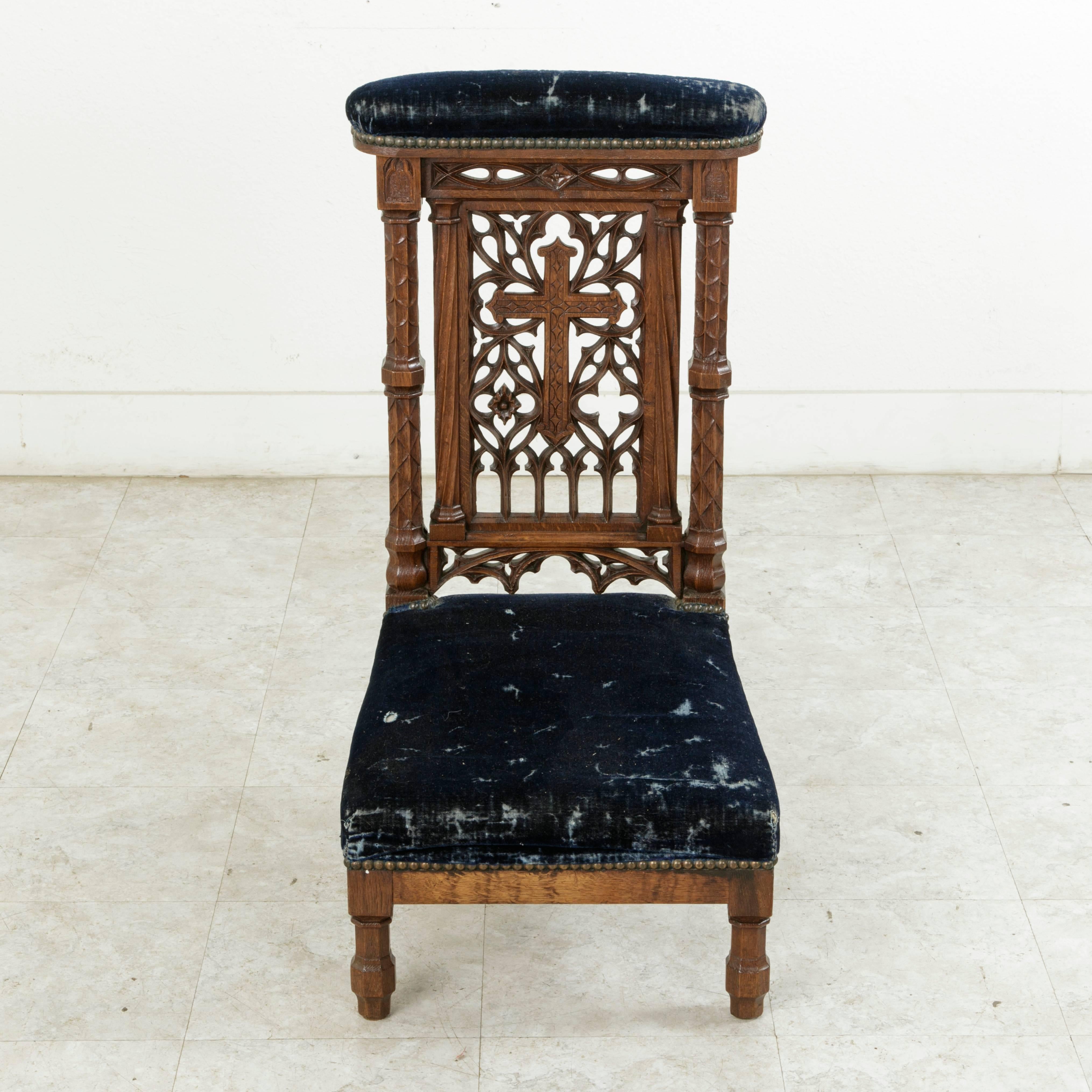 This late 19th century French oak prayer chair, or prie-dieu in French, features delicately hand-carved Gothic elements and a central cross flanked by twisted fluted columns. Two additional columns at the sides are decorated with stylized water