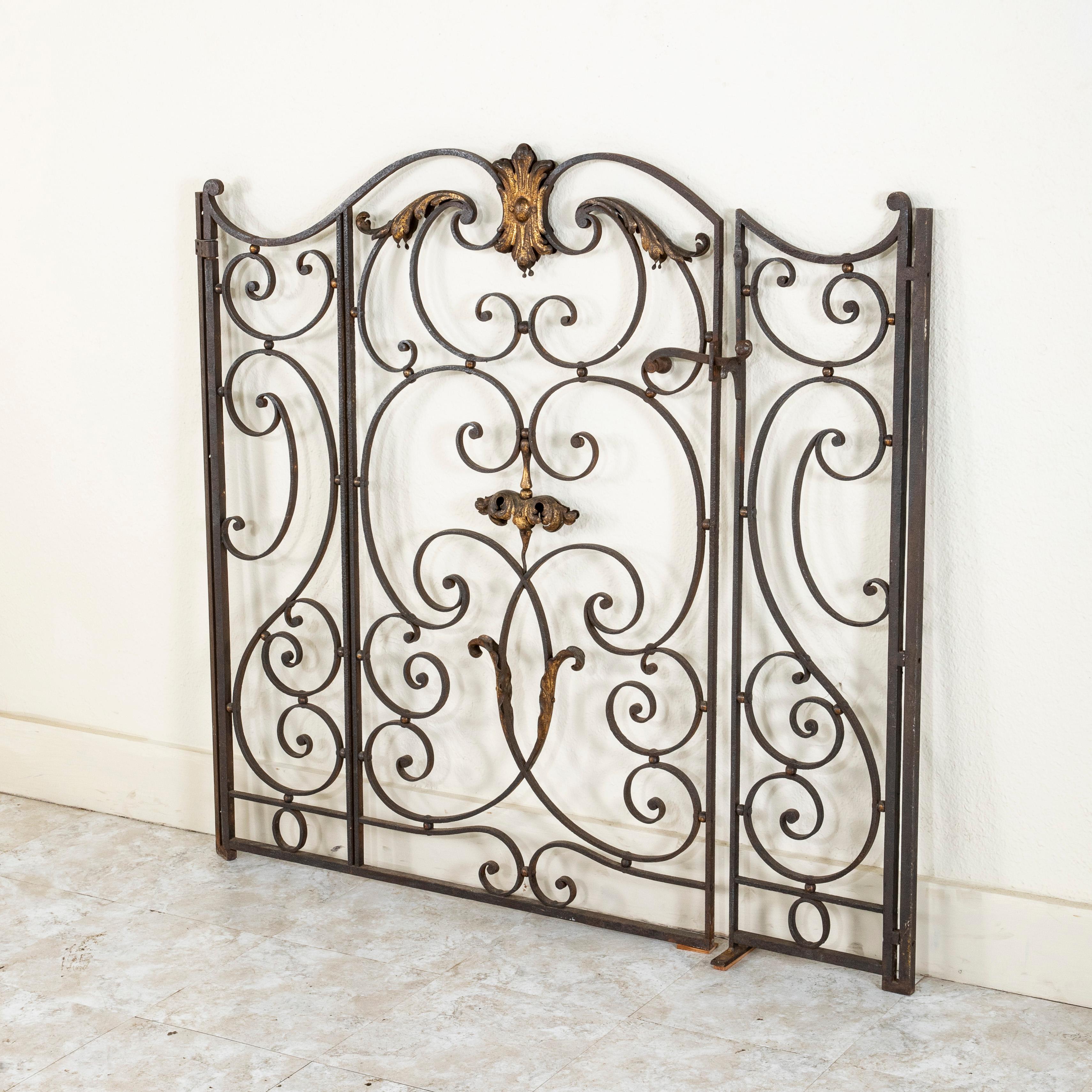 This French hand forged iron double faced gate from the late nineteenth century features a graceful symmetrical design. A central gilt metal cartouche and stylized leaves enhance its intricately scrolled detailing, and a hinged latch fastens the