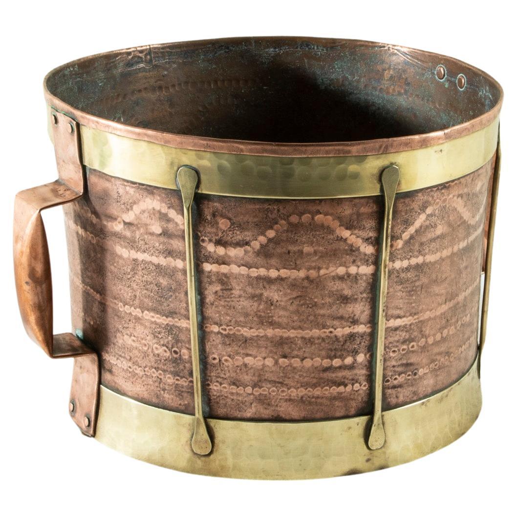 This late nineteenth century French copper vessel features a hand hammered cylindrical form and copper riveted handles. Brass straps encircle the base and upper rim and are joined by brass supports. Its bottom is concave which would have allowed for