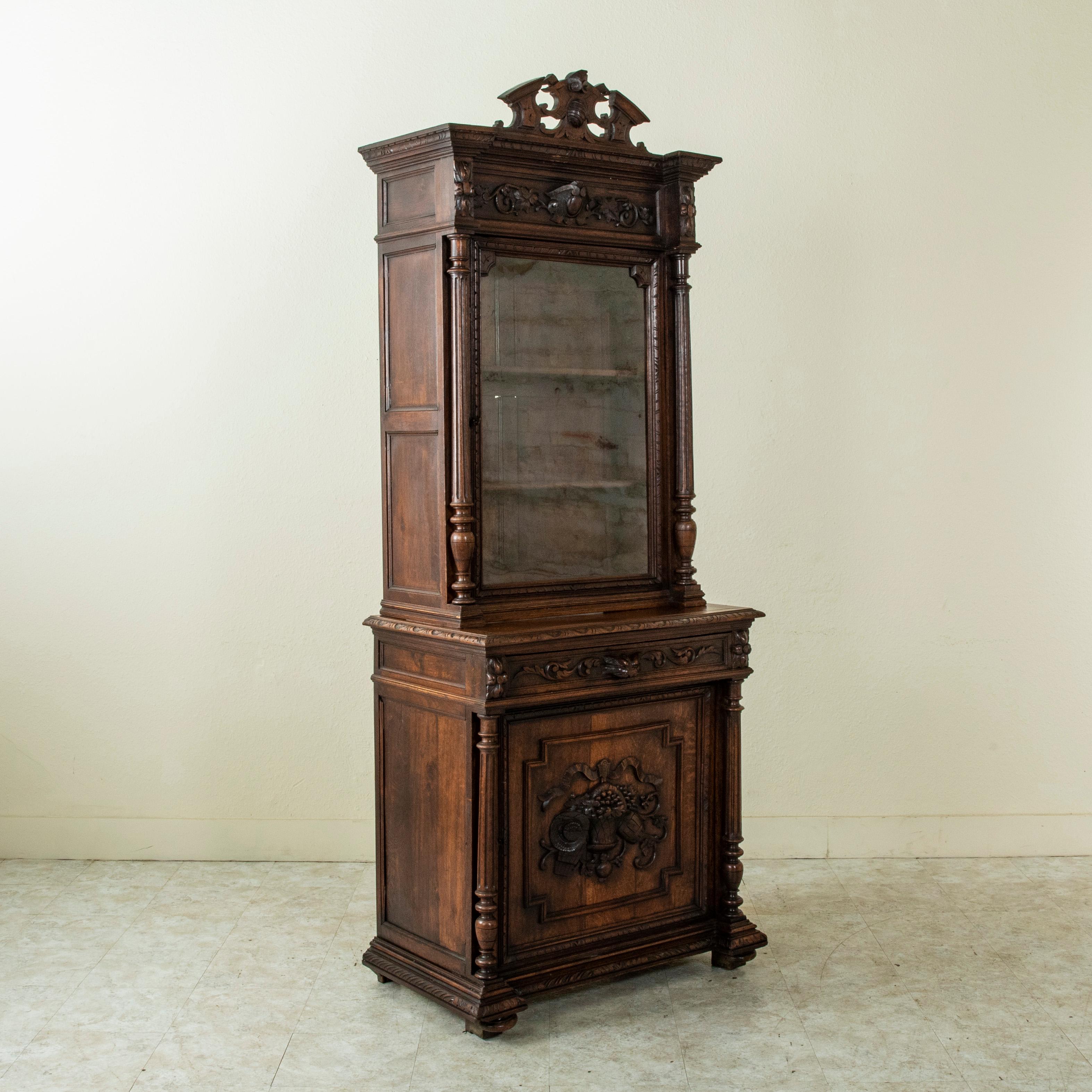 This French oak Henri II style buffet deux corps bookcase from the late nineteenth century features detailed hand carvings of a basket, barrel, and straw hat on the lower door. The upper cabinet displays a central cartouche at its crown flanked by