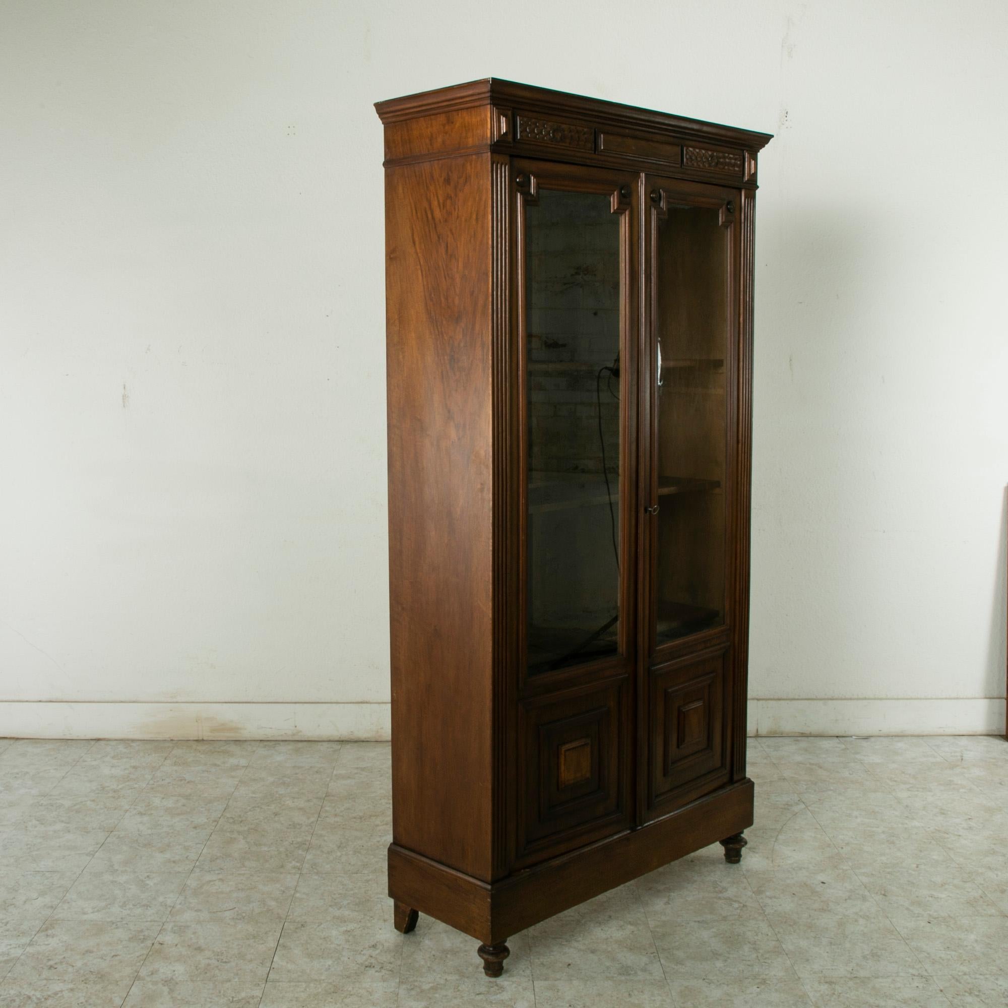 This small scale late nineteenth century Henri II walnut bibliotheque or bookcase rests on finial feet and features fluted columns flanking its glass doors. A simple diamond carving adorns the corners of its upper transom, and panels with rosettes