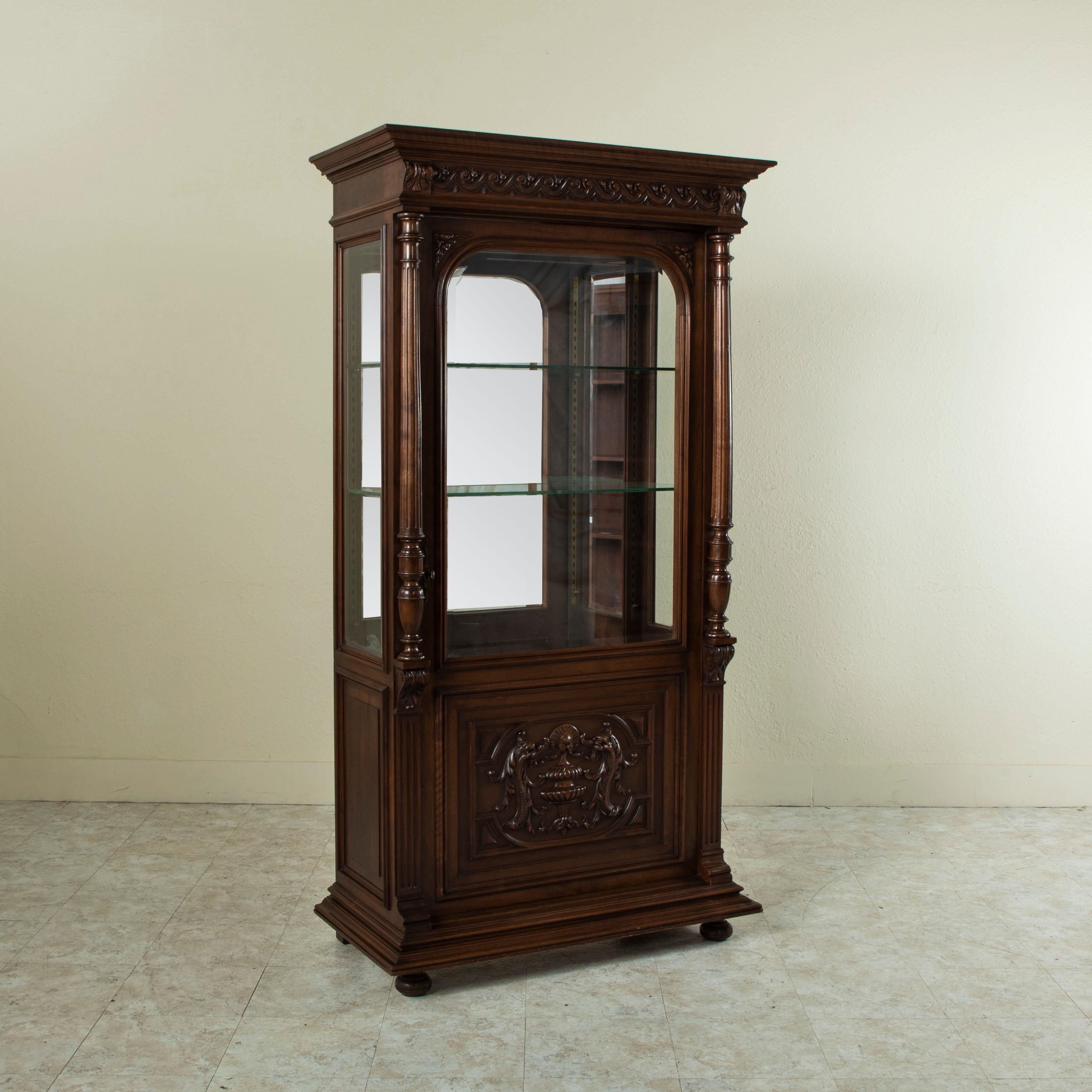 This late nineteenth century French Henri II vitrine is constructed of hand-carved walnut and features beveled glass on three sides. Hand carved acanthus leaves detail the sides and corners and two fluted columns frame the door. The lower panel of