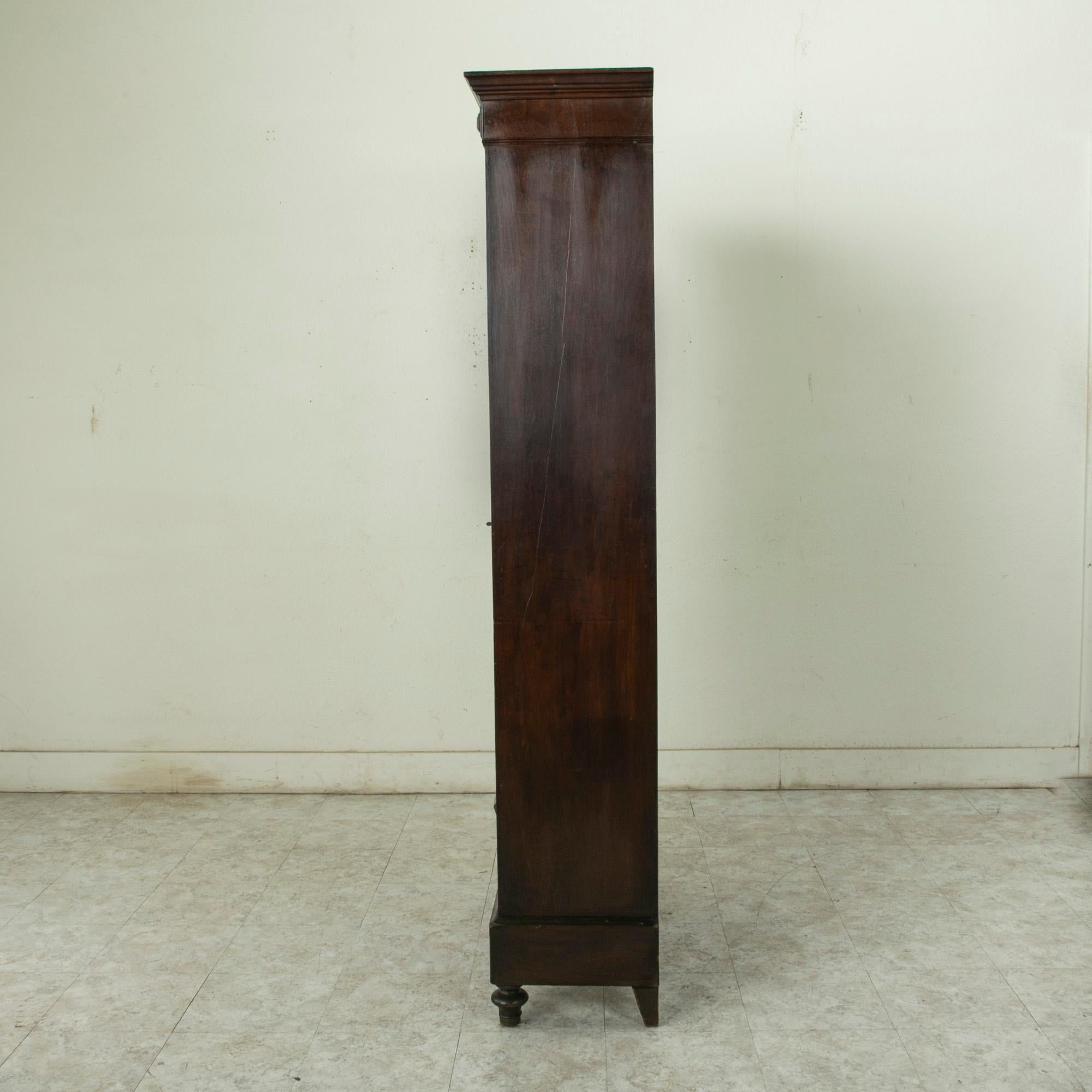 This small scale late nineteenth century Henri II walnut bibliotheque or bookcase rests on finial feet and features fluted columns flanking its original hand blown glass doors. A simple diamond carving adorns the corners of its upper transom, and