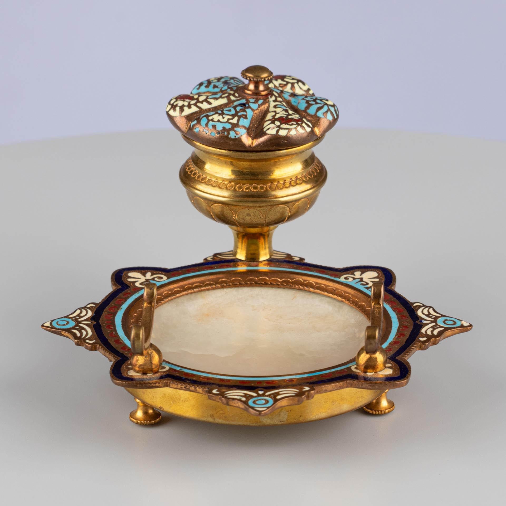 Calamaio con decorazione a smalto e piatto in onice

Origine: Probabilmente Francia
Materiale: Metallo dorato, smalto champlevé, onice
Data: Circa 1870-1890

Dimensioni:
H. H. × L. × P.: 9 × 12 × 13 cm.

Descrizione:
Questo elegante calamaio da