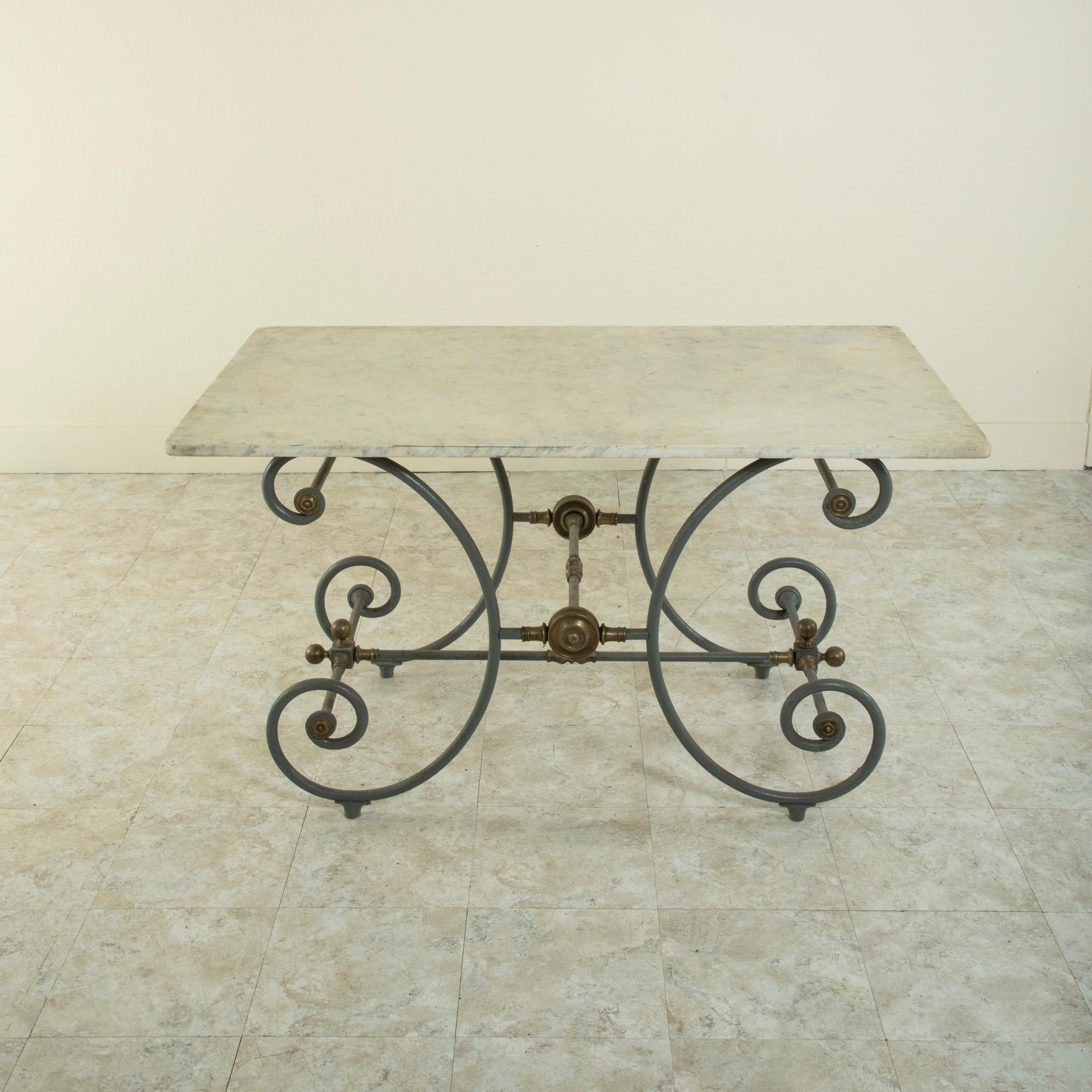 This late nineteenth century French iron pastry table or butcher's table features a solid carrara marble top. The marble rests on a scrolled, painted iron base. Brass medallions and finials adorn the supports connecting the legs. Ideal for use as a
