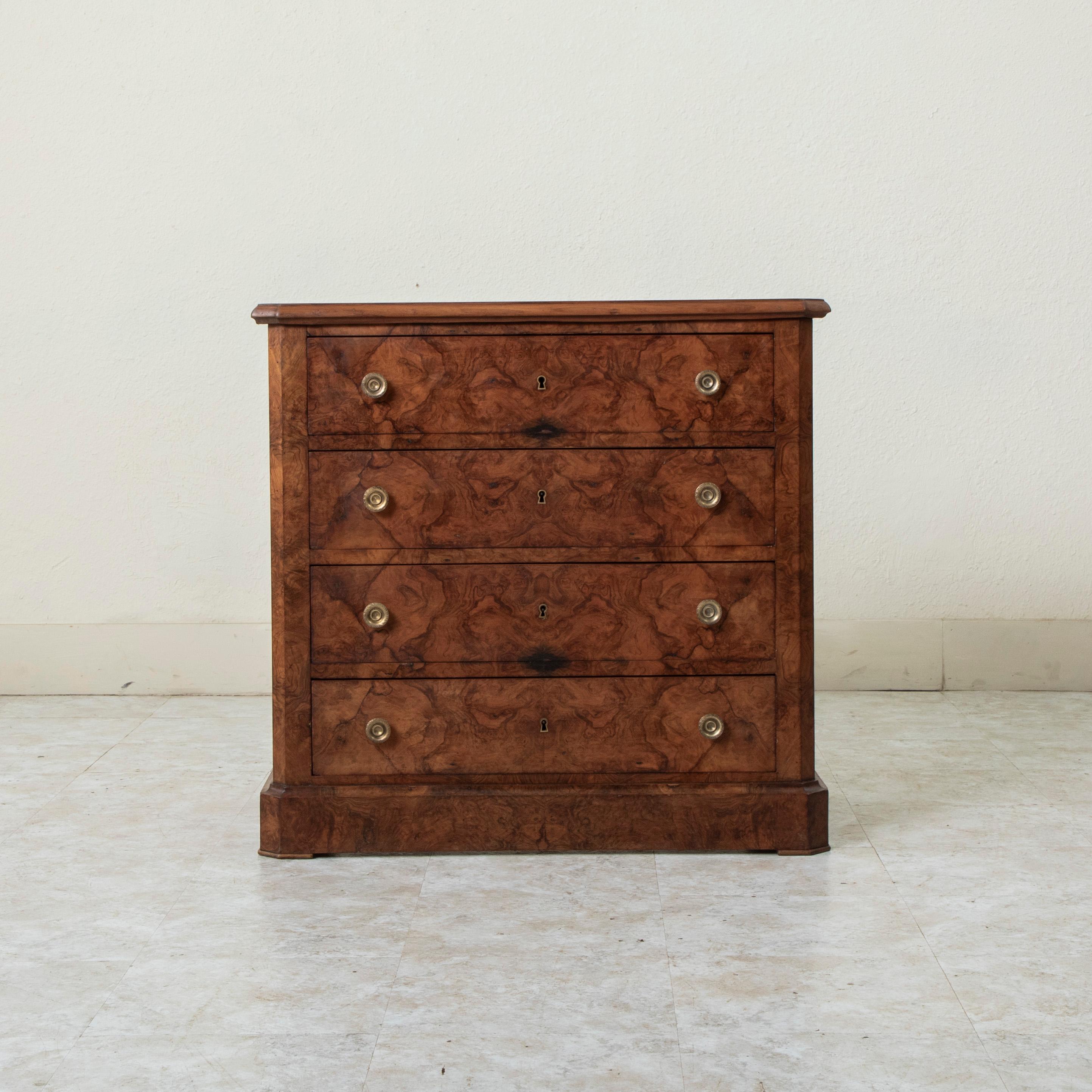 Rare for its smaller scale with a 31 inch width, this late nineteenth century Louis Philippe style commode or chest of drawers features a facade of book matched burl walnut. Its four drawers of dovetail construction are each appointed with a pair of
