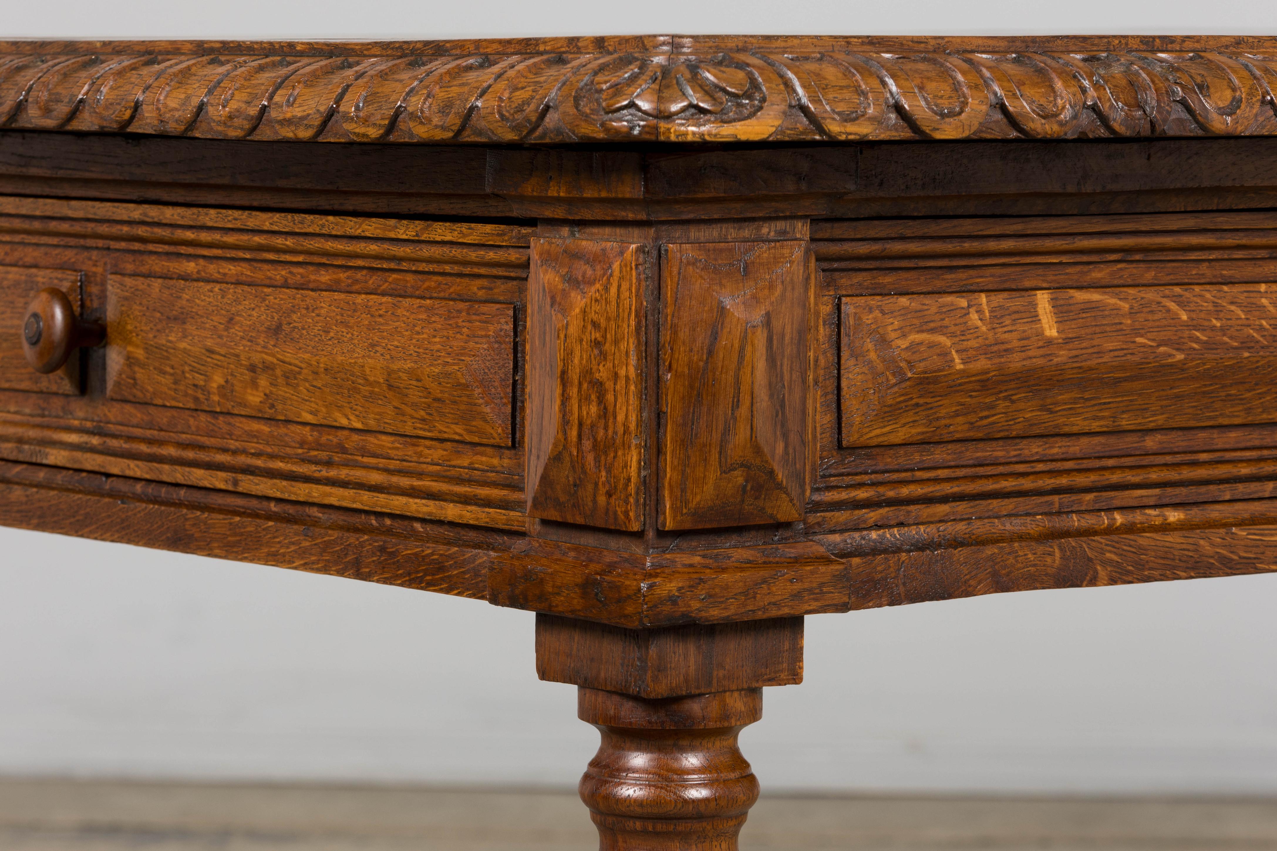 A late 19th-century French Louis XIII style writing table, sourced in Provence. Crafted in solid oak with well-defined grain, the table features a molded top with carved egg-and-dart edging and an architectural apron with paneled details. Turned