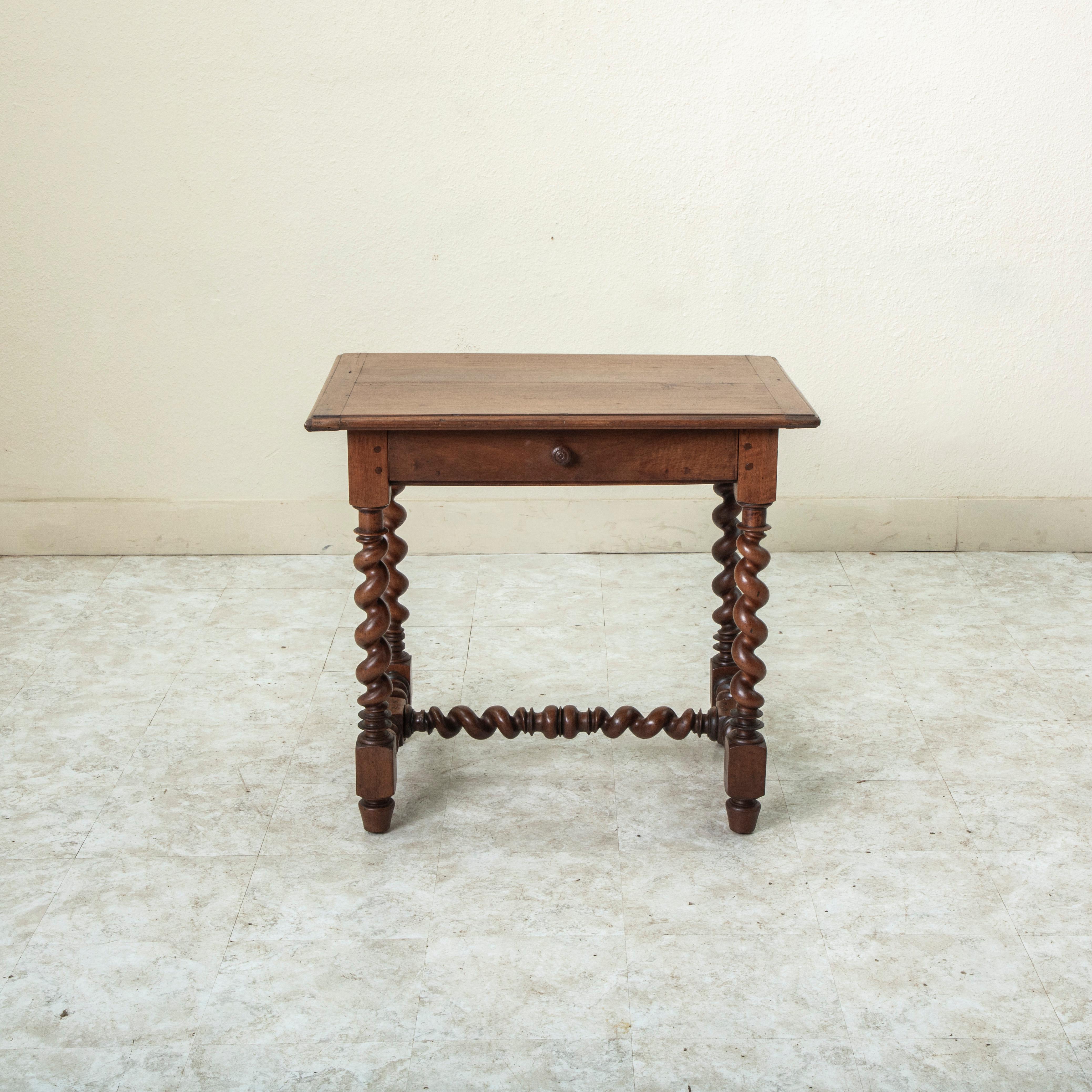 This small scale French Louis XIII style walnut writing table or desk from the late nineteenth century is of hand pegged construction and features a beveled top. The top is supported by barley twist legs that rest on finial feet. A barley twist