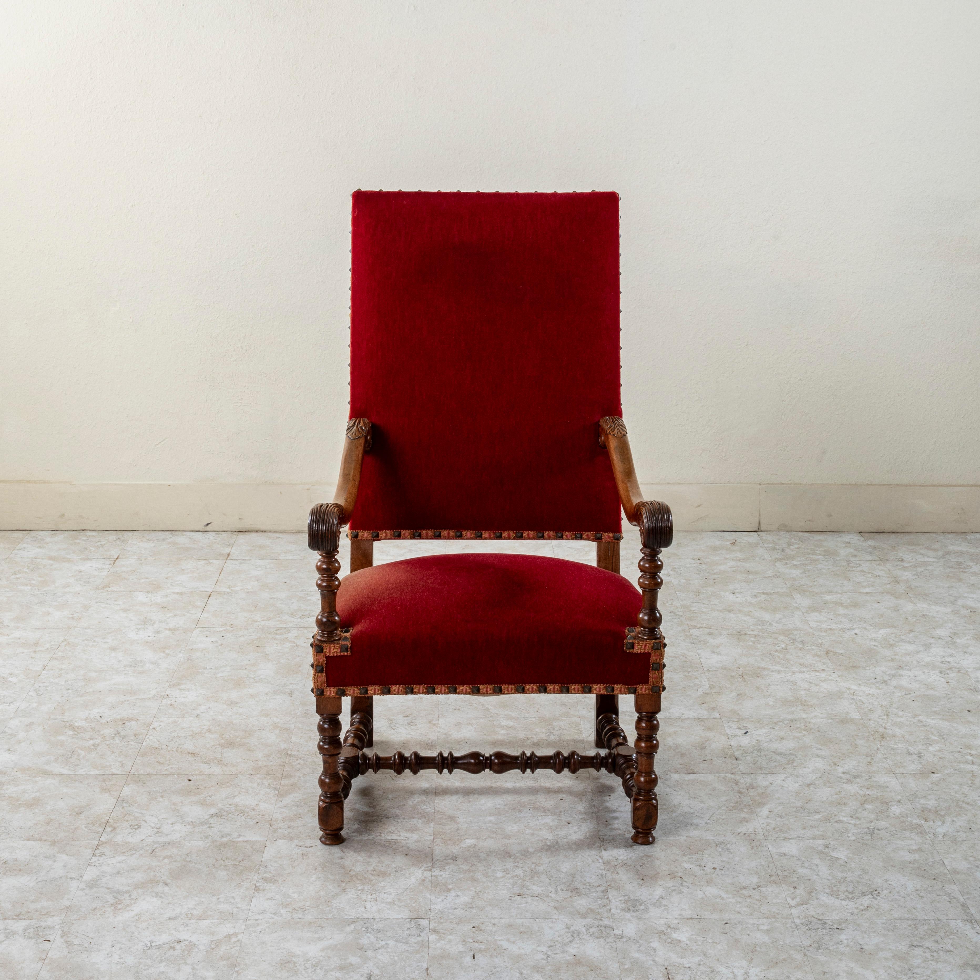 Questa poltrona francese di fine Ottocento in noce intagliato a mano in stile Luigi XIV presenta braccioli intagliati a mano con foglie d'acanto a scorrimento. Il sedile poggia su gambe a rocchetto unite da una staffa ad H. che ne garantisce la