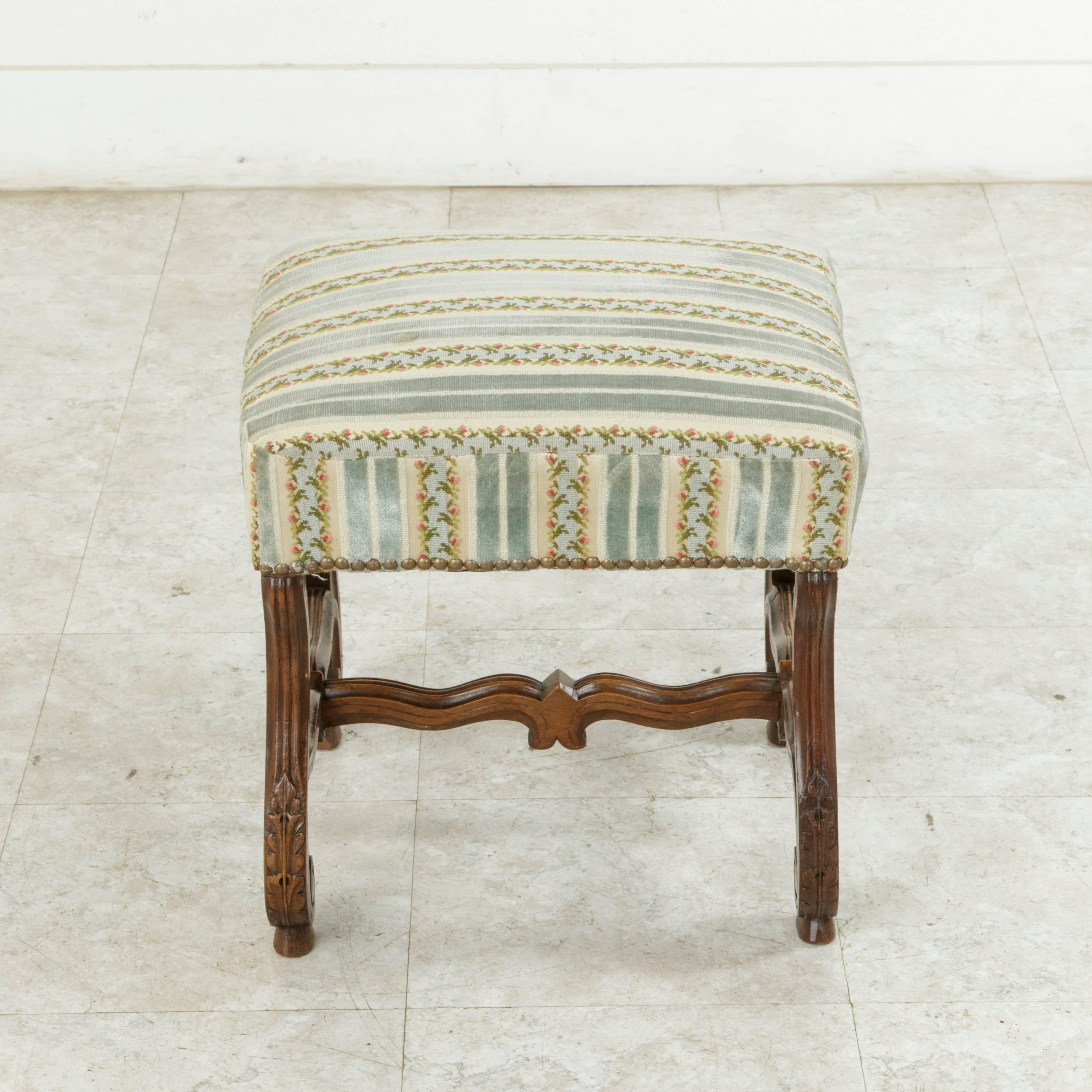 This late 19th century French Louis XIV style banquette or vanity bench features fluted and scrolled mutton legs detailed with hand-carved acanthus leaves. A curved H stretcher joins the legs and provides stability to the stool. Upholstered with