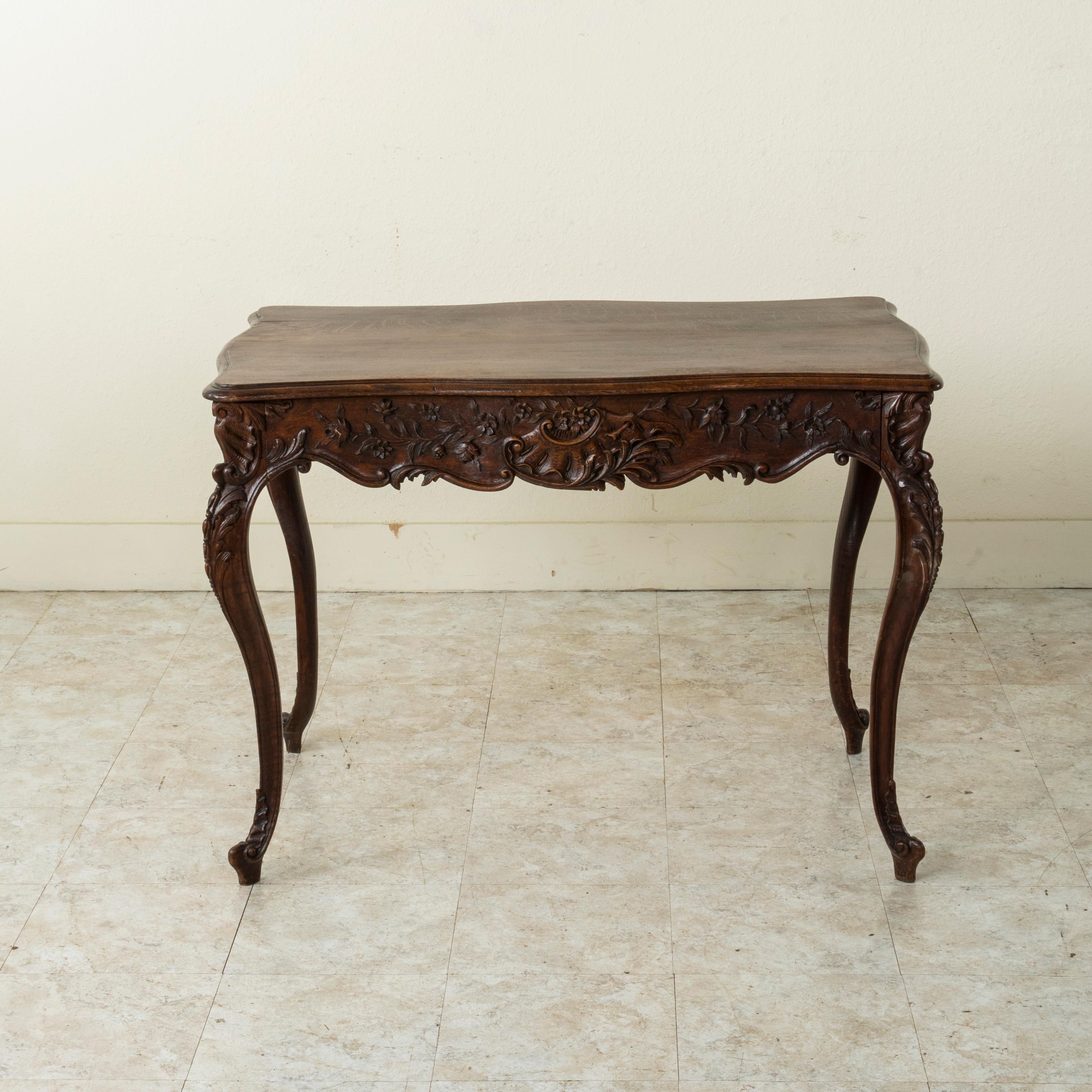 This late nineteenth century French Louis XV style oak writing table or desk features deep relief hand carved details of shells on all four sides and corners as well as scrolling leaves and a floral motif. A single drawer of dovetail constructions