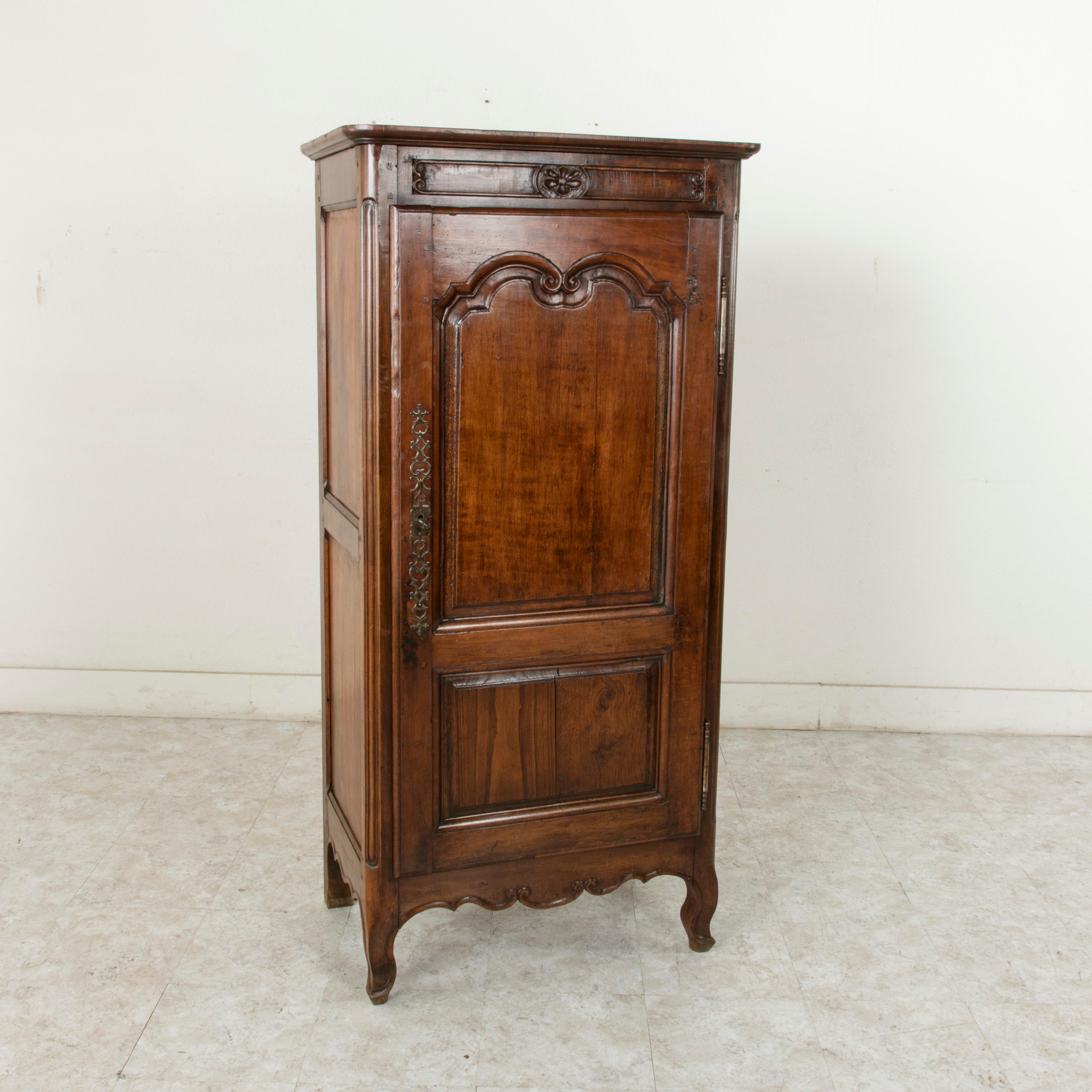 This small scale late 19th century French Louis XV style bonnetiere or cabinet is constructed of solid walnut with hand pegged paneled sides and hand carved scrolling details. A central deep relief hand carved flower adorns the top below the