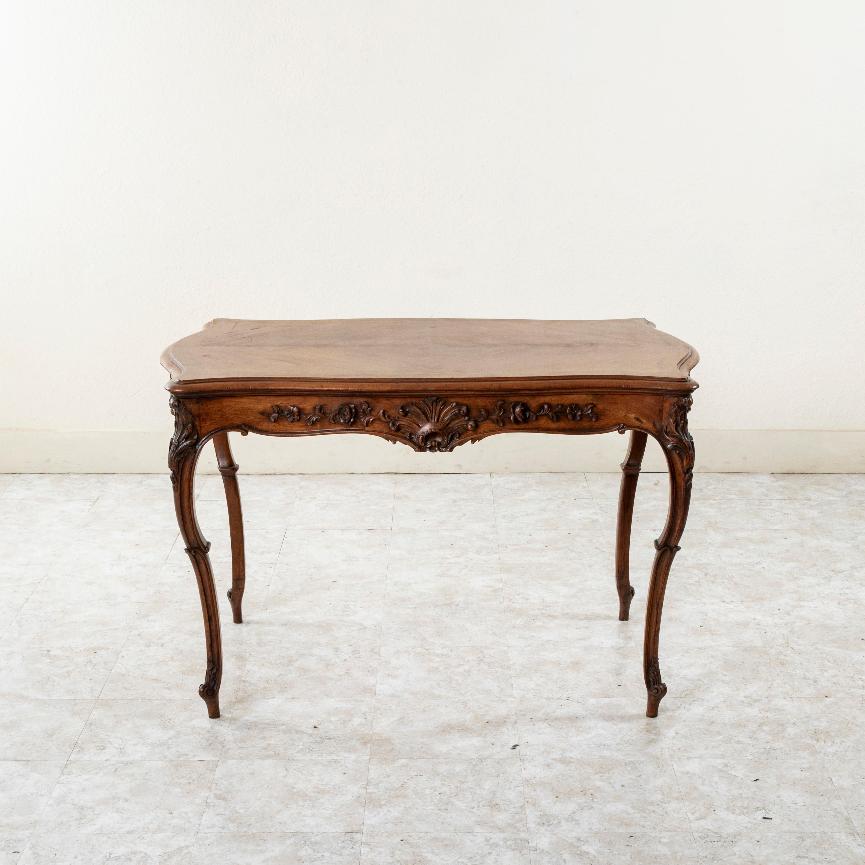 This late nineteenth century French Louis XV style walnut writing table or desk features deep relief hand carved details of shells on all four sides and corners as well as scrolling leaves and a floral motif. A single drawer of dovetail construction