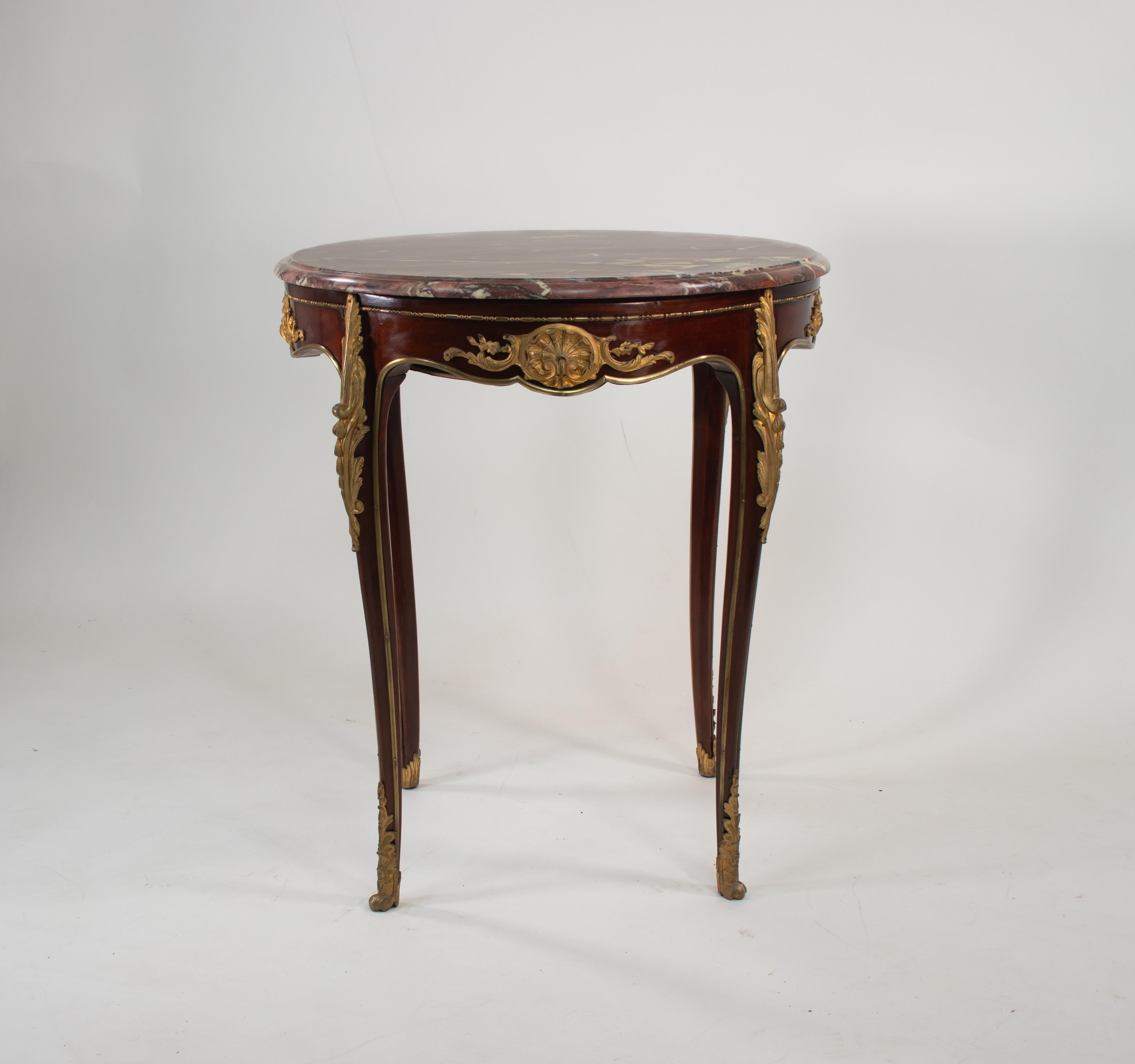 Cette magnifique table en marbre rose de style Louis XV est faite d'acajou et de détails dorés. Elle repose sur de minces pieds cabrioles terminés par de fins sabots en laiton. Le plateau de la table ronde est composé d'un magnifique marbre rose