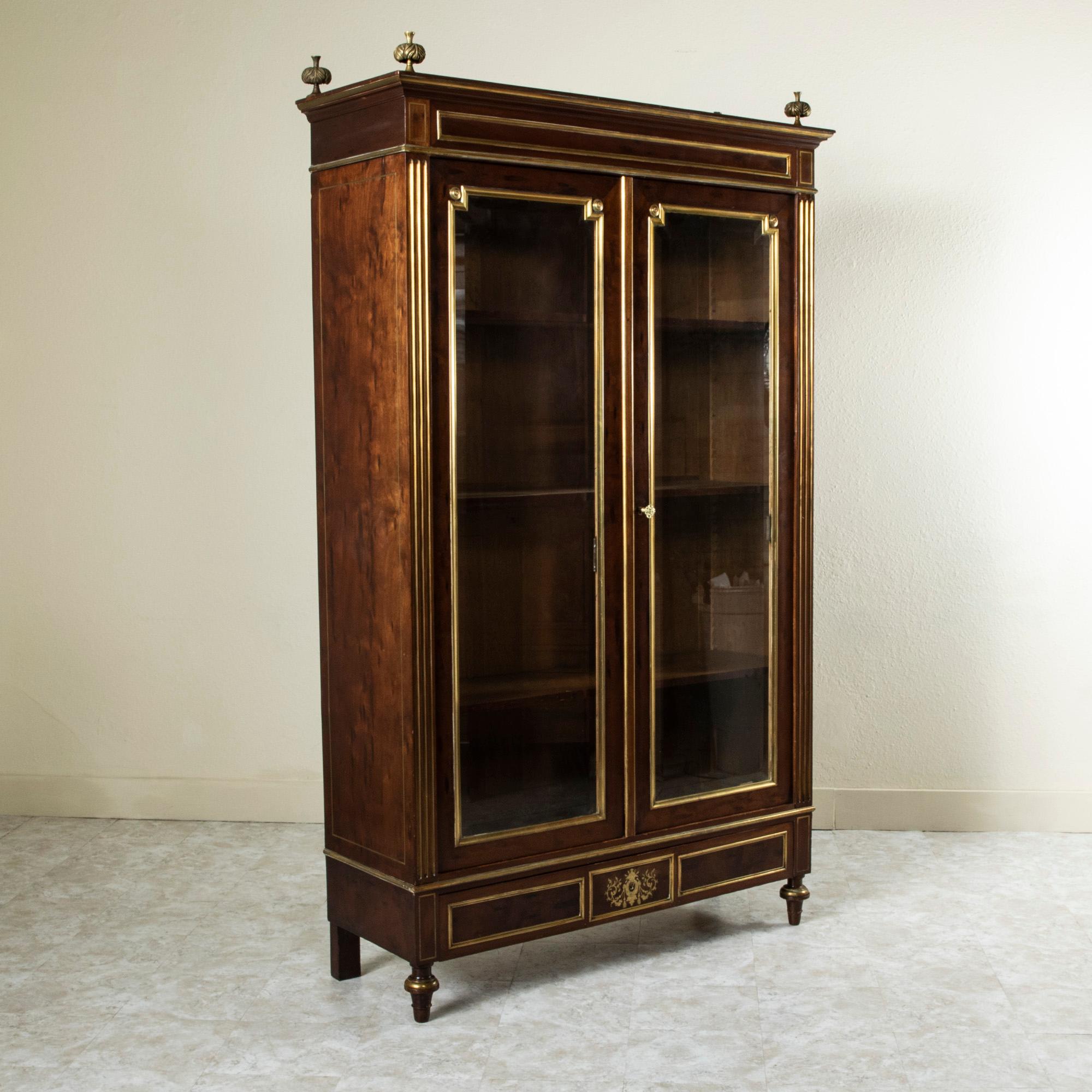 This late nineteenth century Louis XVI mahogany Bibliotheque or bookcase is finished in stunning bronze banding. Bronze-fluted corners flank its two beveled glass doors. The doors open to reveal an interior fitted with four adjustable interior