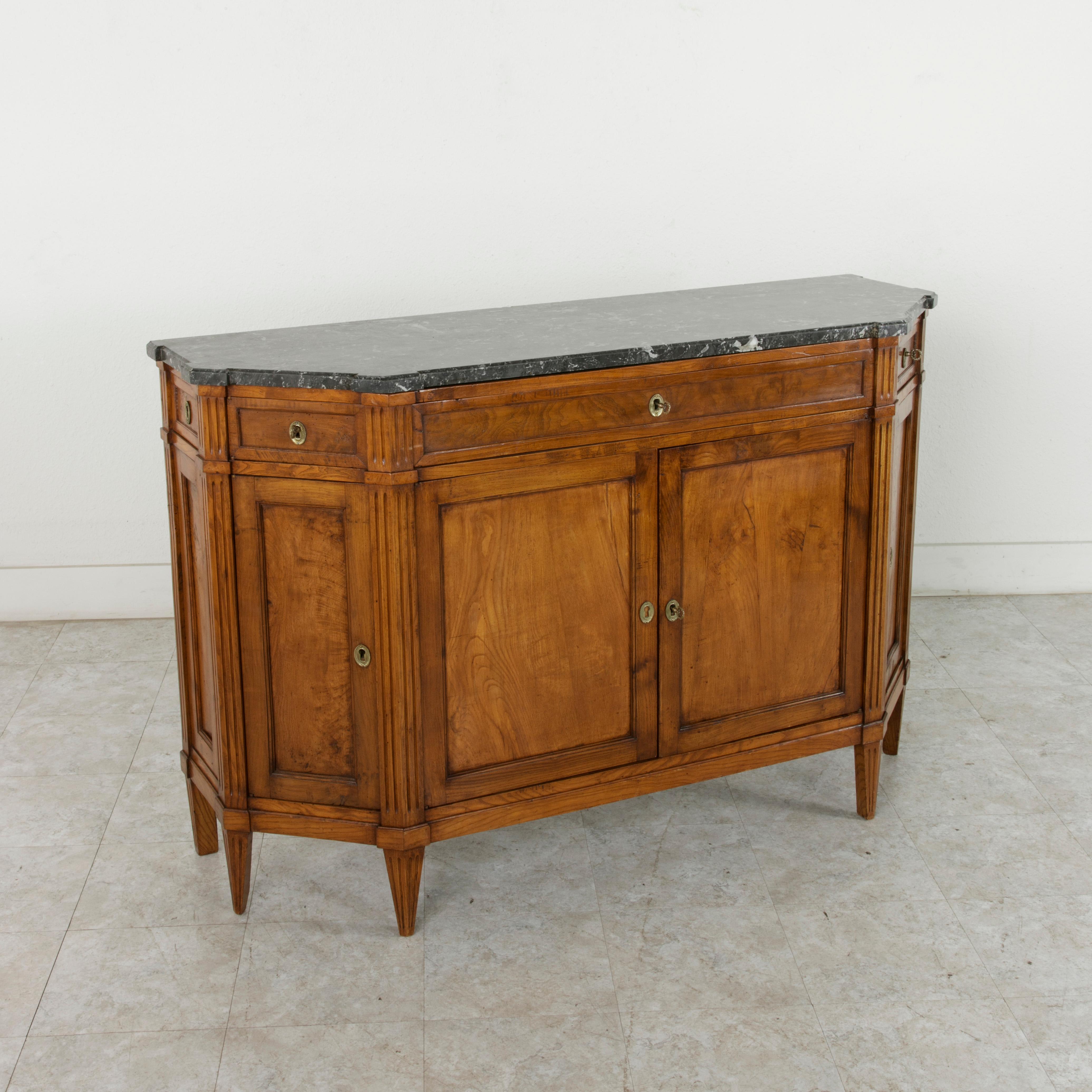 Found in Paris, France, this late 19th century Louis XVI style enfilade, sideboard, or buffet features a rare five-sided ashwood facade with a beveled Saint Anne marble top. The piece has Classic Louis XVI fluted corners and rests on tapered fluted