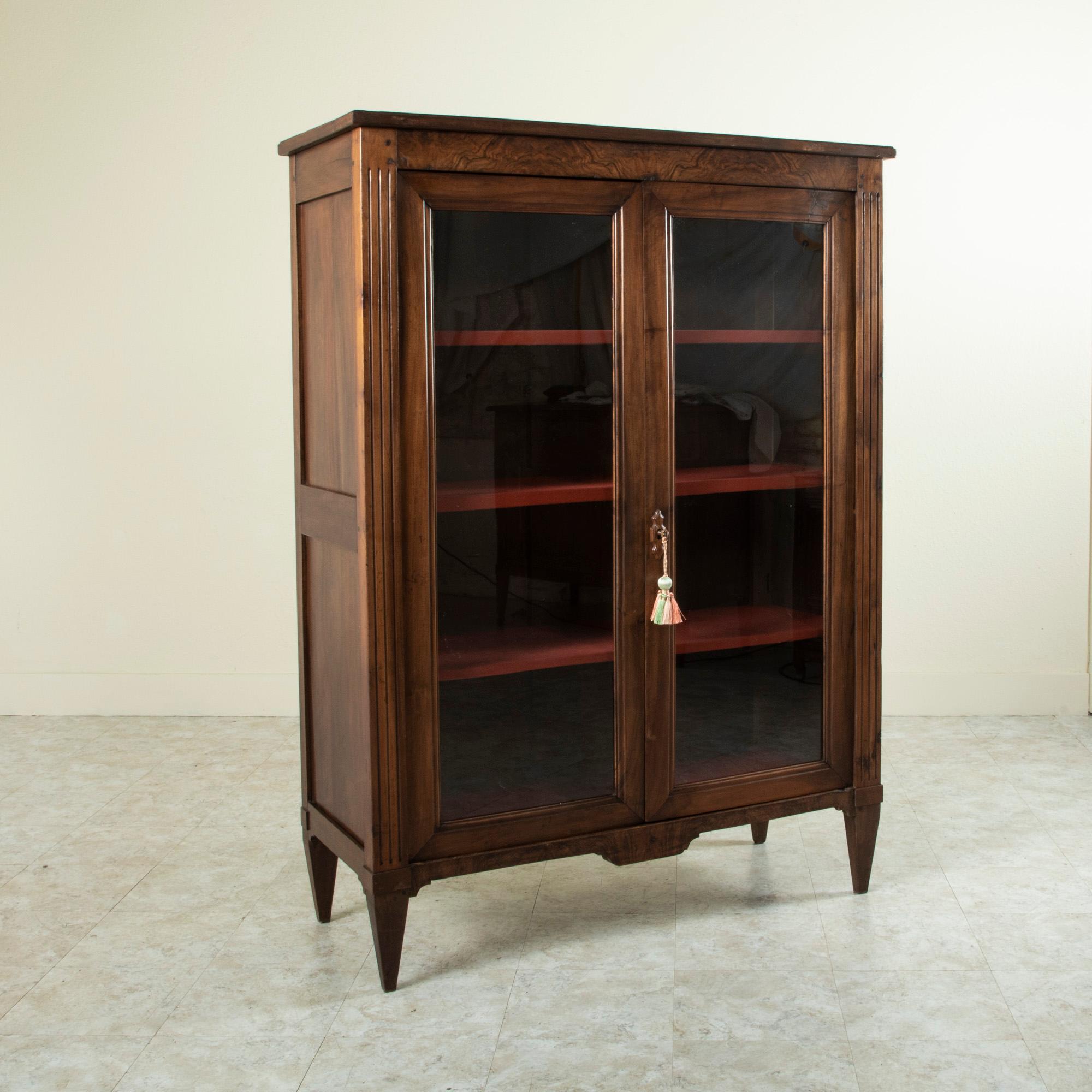 This late nineteenth century French Louis XVI style hand pegged walnut bookcase or vitrine features fluted corners that lead to tapered legs. Each side is constructed of solid walnut panels and the front is constructed of book matched burl walnut.