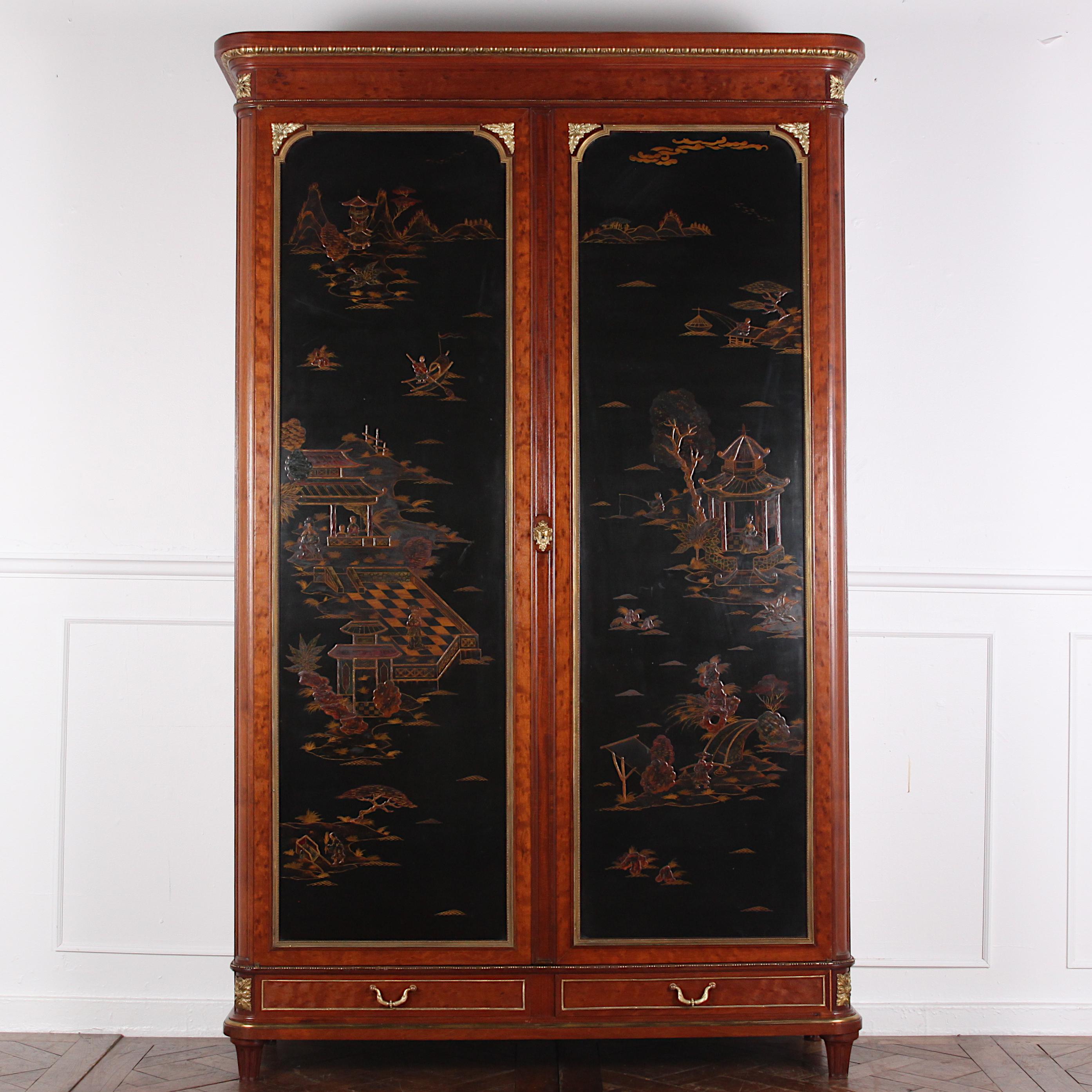 A lovely-quality and highly unusual late 19th century French Louis XVI style two-door armoire featuring dramatic ‘Japanned’ door panels in black lacquer with landscape and architectural scenery in colored lacquer and gilding. The contrasting case in