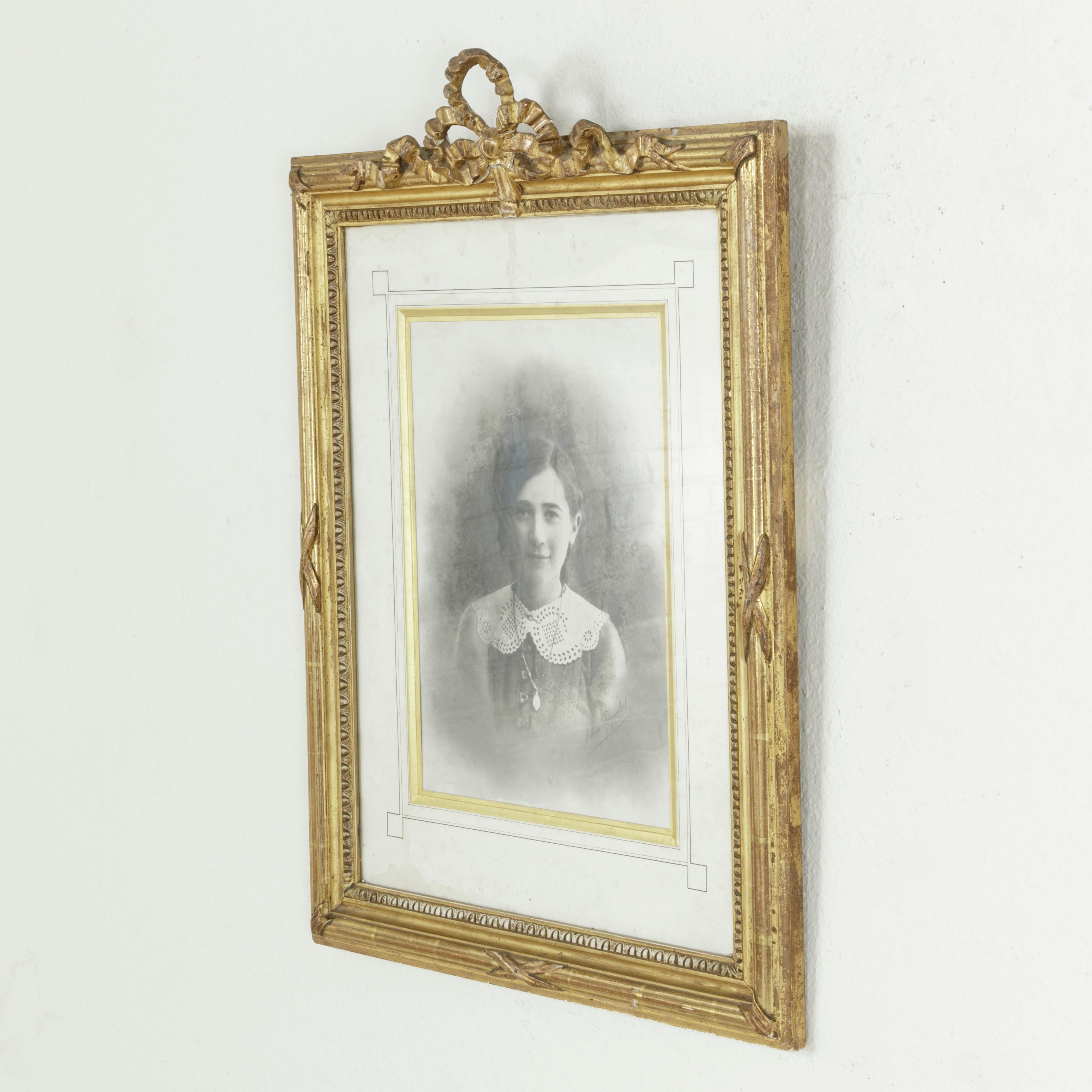 This late nineteenth century French Louis XVI style gilt wood frame features a classic knotted ribbon at the top. The frame is additionally detailed with a crossed ribbon motif and the inner part of the frame has an egg and dart pattern. In the