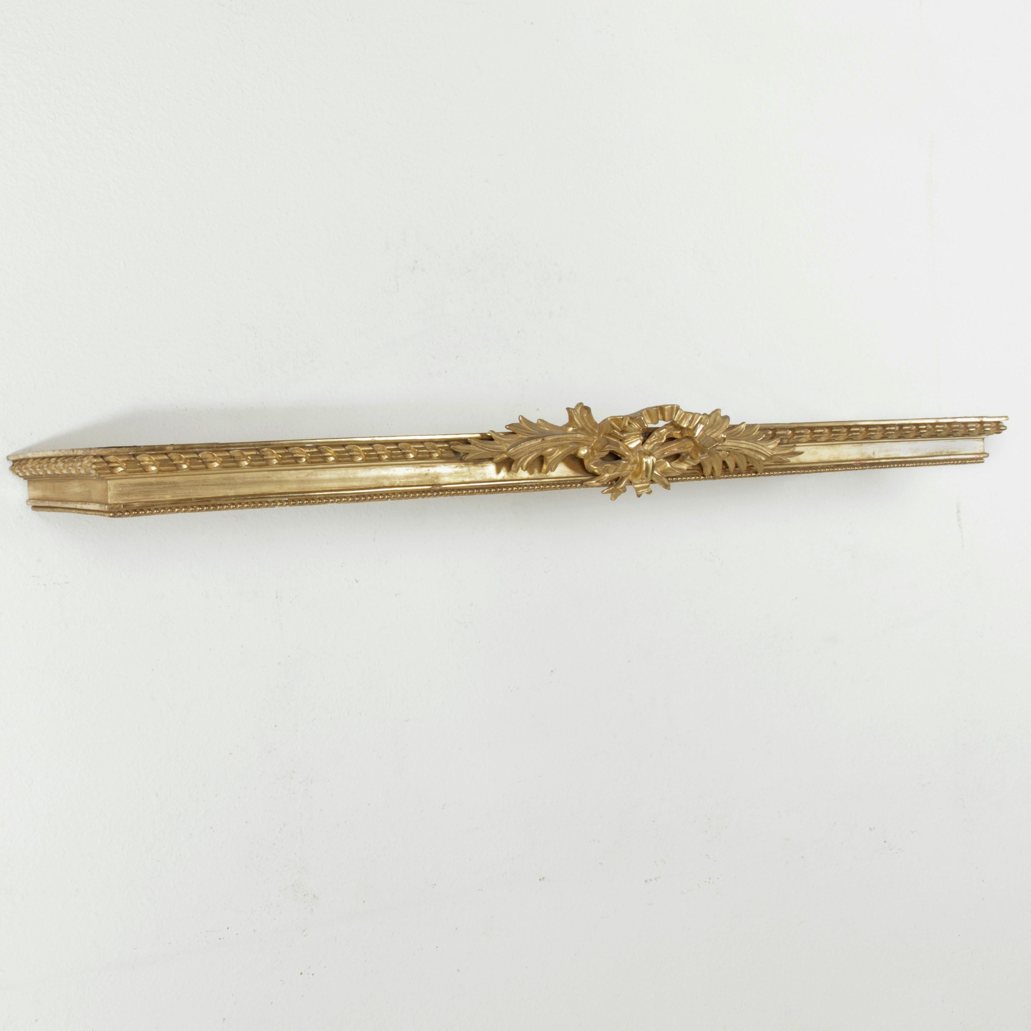 This stunning late 19th century window cornice of hand carved giltwood was originally used as a drapery valance in a French chateau. It features a Classic Louis XVI motif of a knotted bow and ribbon with crossed palm fronds. The upper and lower
