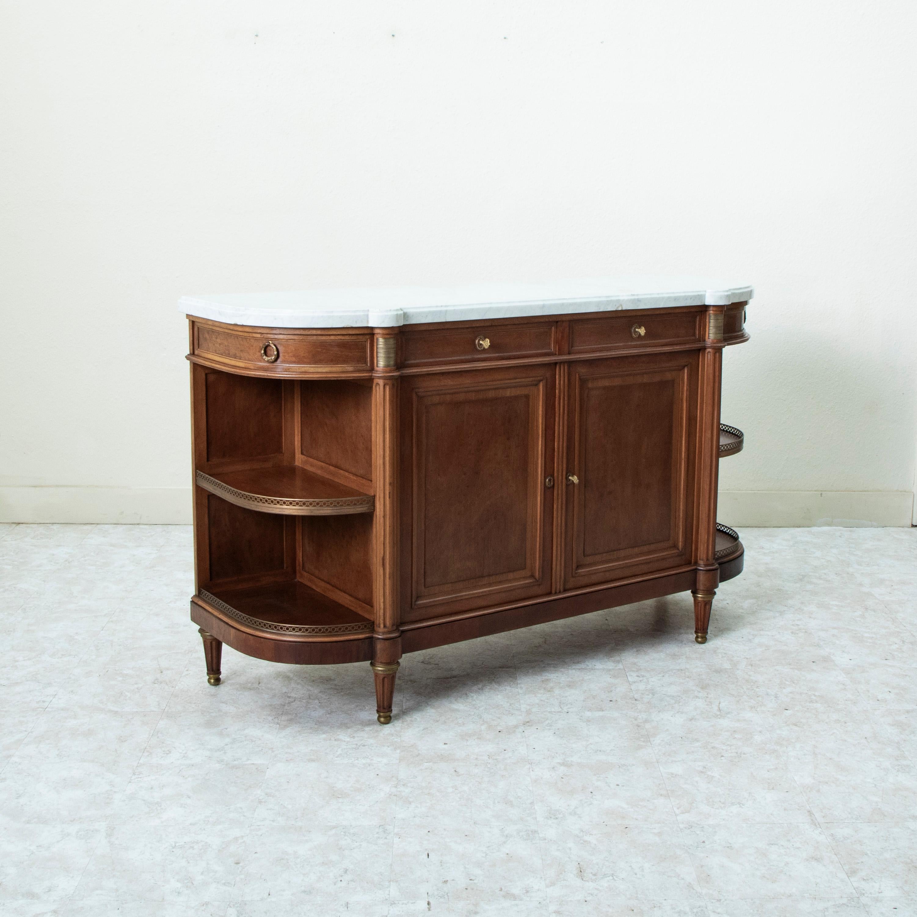 This late nineteenth century French Louis XVI style mahogany demi-lune enfilade, sideboard, or buffet features a 1.5 inch thick beveled white marble top and bronze detailing. This piece has four drawers of dovetail construction fitted with bronze