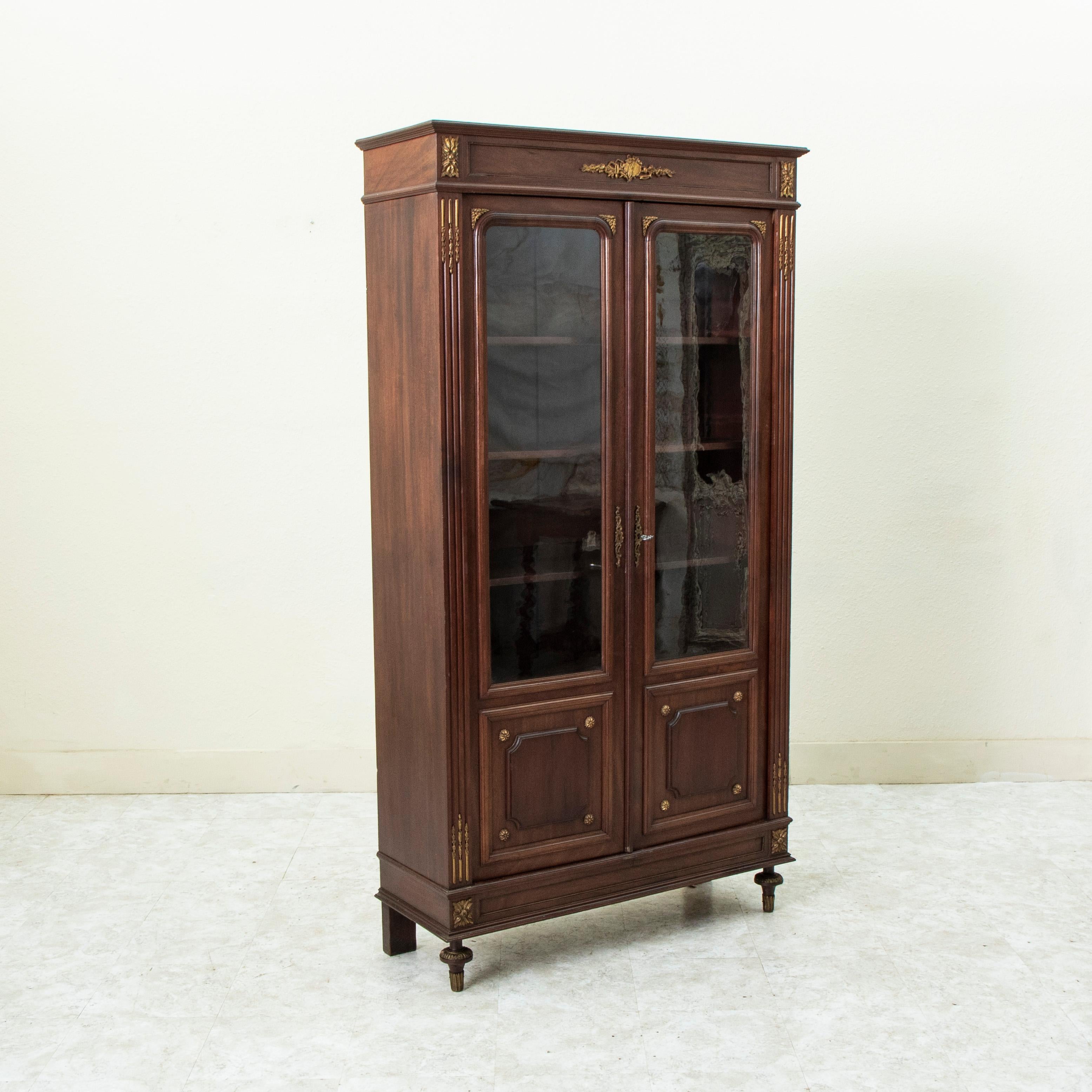 Questa bibliotheque o libreria in mogano in stile Luigi XVI della fine del XIX secolo presenta dettagli in bronzo con rosette sulle giunture e una placca sulla corona con un motivo floreale e strumenti musicali. I suoi angoli sono caratterizzati da