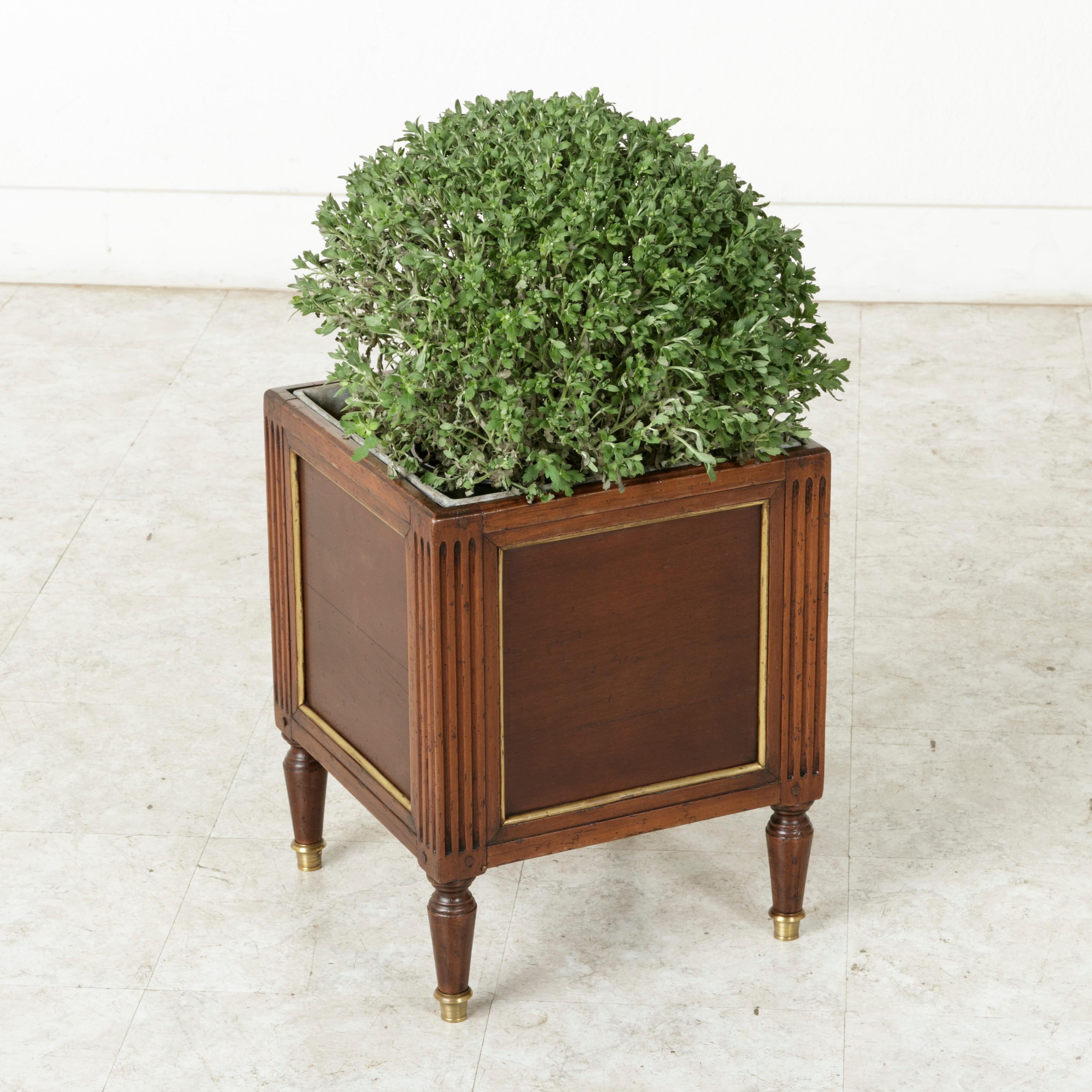 This French Louis XVI style mahogany square planter or jardinière from the late 19th century features bronze trim around each of its paneled sides. Classic fluted corners rest on tapered legs finished with bronze sabots. Its original zinc liner has