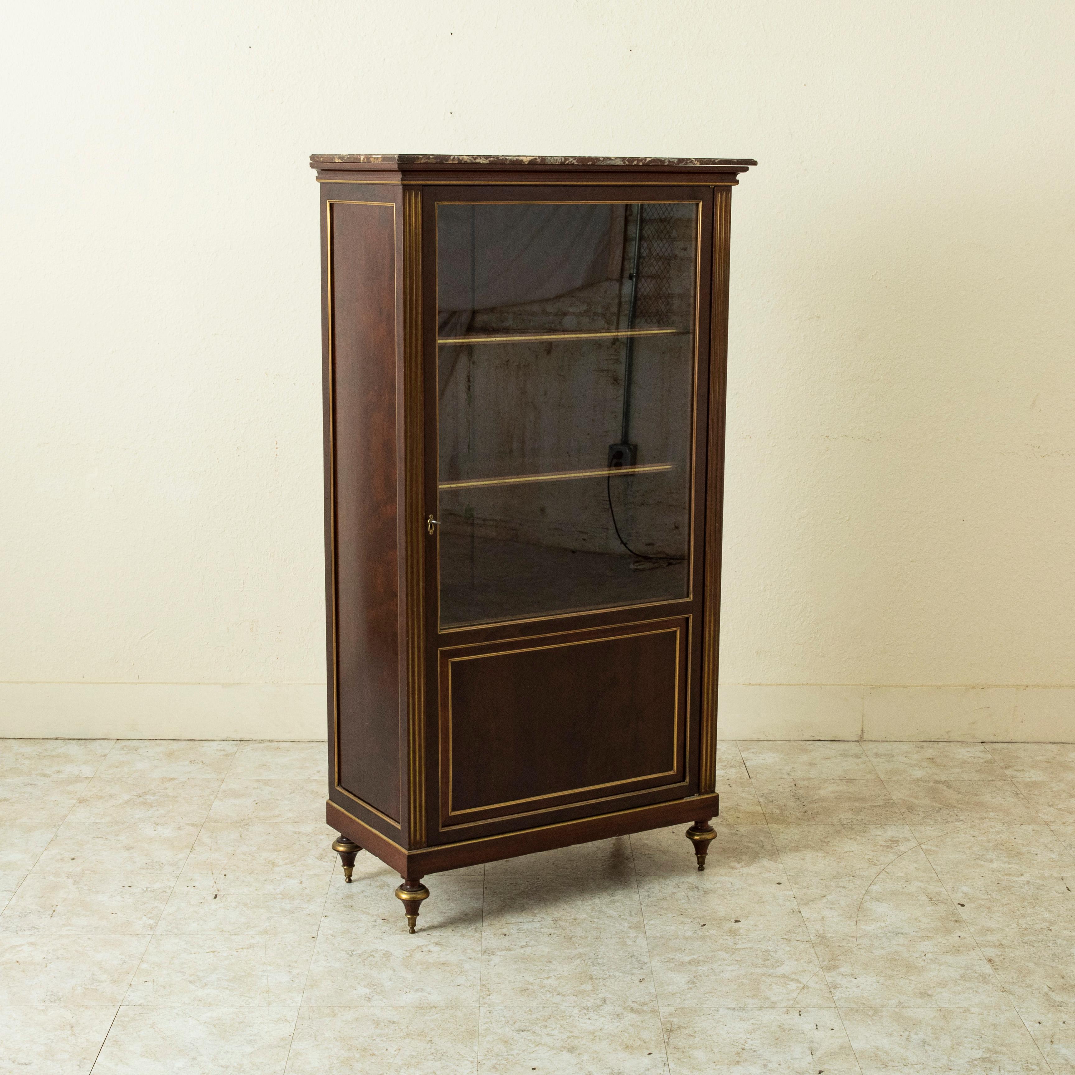 D'une hauteur de 58 pouces, cette petite vitrine ou bibliothèque en acajou de la fin du XIXe siècle, de style Louis XVI, est ornée de superbes bandes de bronze et d'un plateau en marbre rouge veiné de blanc. Ses angles sont dotés de cannelures et de