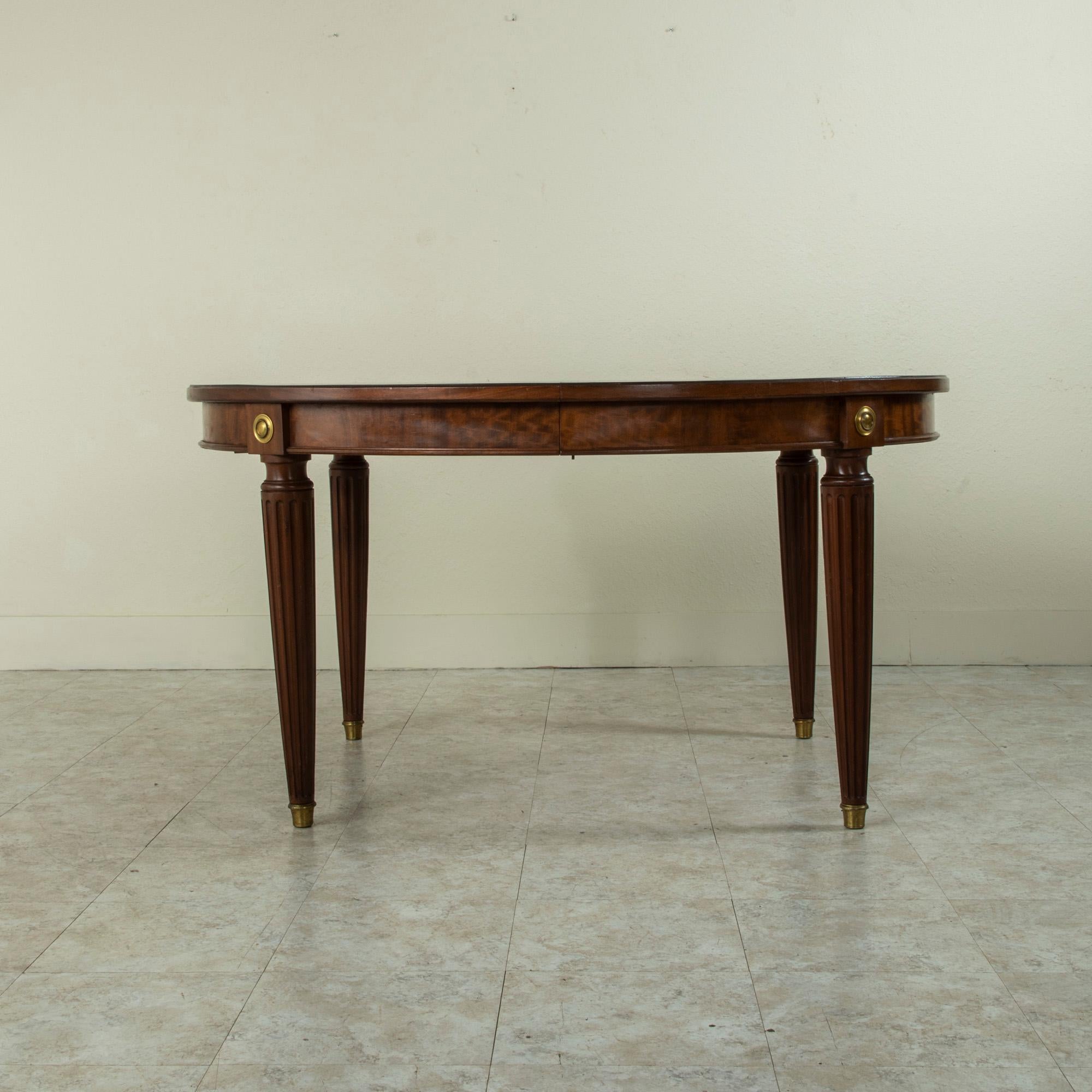 This late nineteenth century French mahogany oval dining table features a beveled top and round bronze medallions detailed with beading at the die joints. The top rests on tapered fluted legs finished with bronze sabots. From floor to apron measures