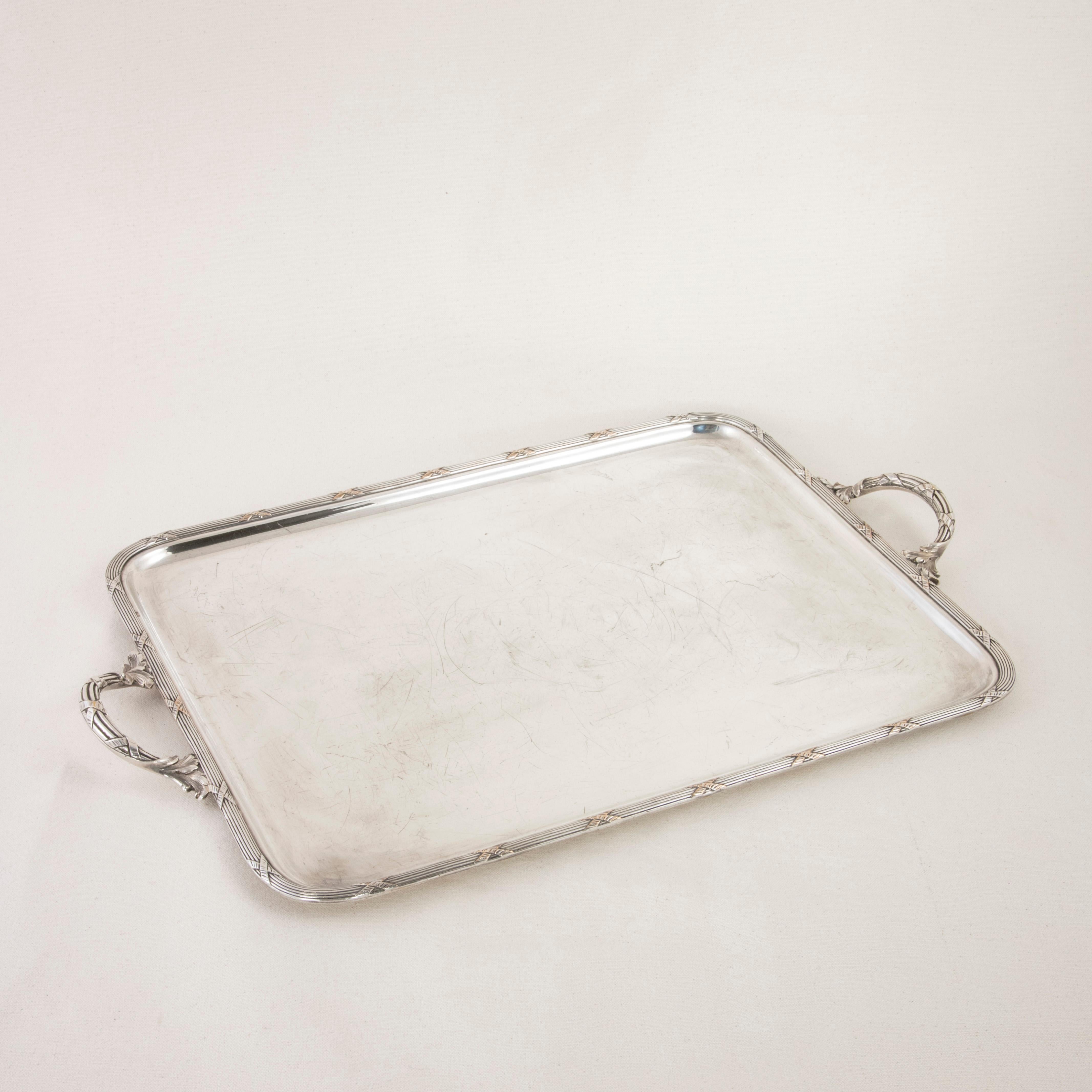 This late nineteenth century French silver plate serving tray features a raised rim with a classic Louis XVI motif of crossed ribbons. A handle at each end repeats the crossed ribbon motif with stylized leaves at the joints. An elegant serving piece