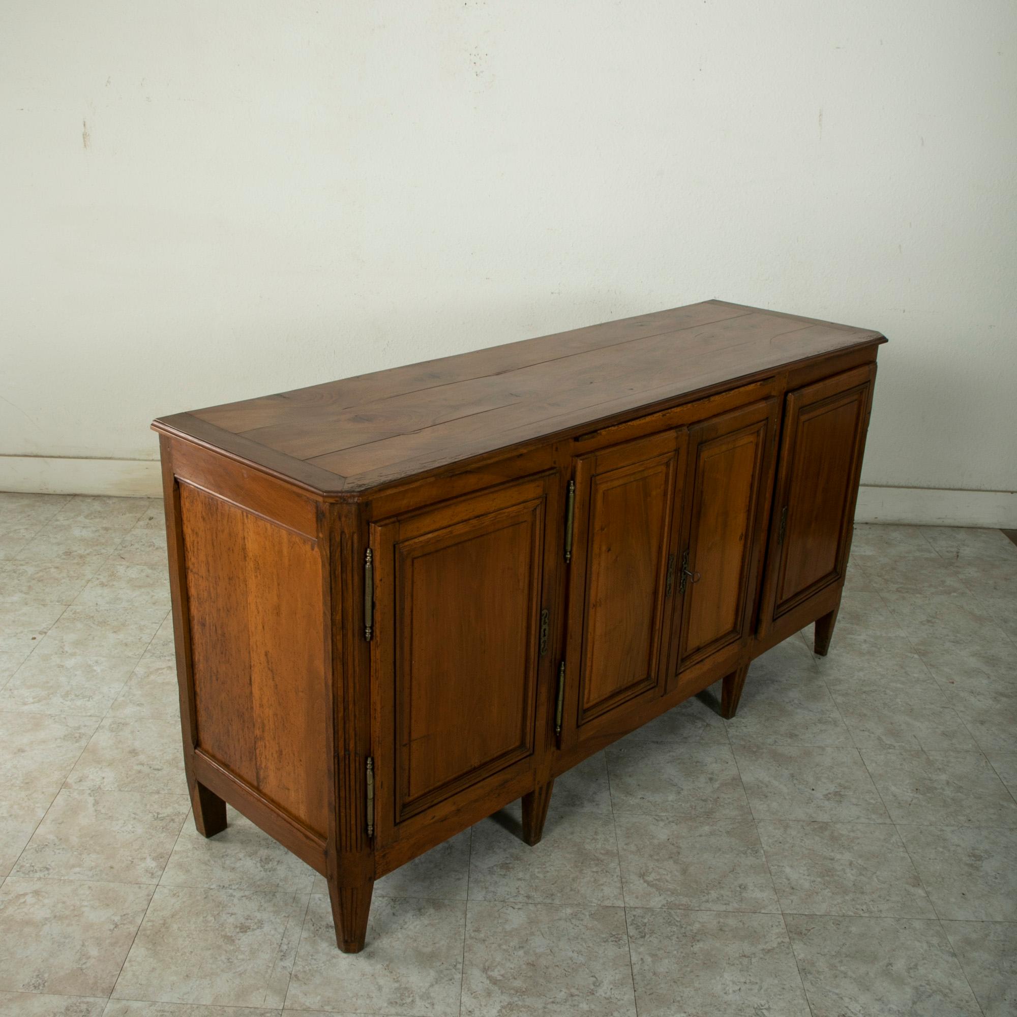 This late nineteenth century Louis XVI style enfilade, sideboard, or buffet is constructed of solid walnut and features a beveled top and central pull out tray. Of hand pegged construction, this piece has classic Louis XVI fluted corners and rests