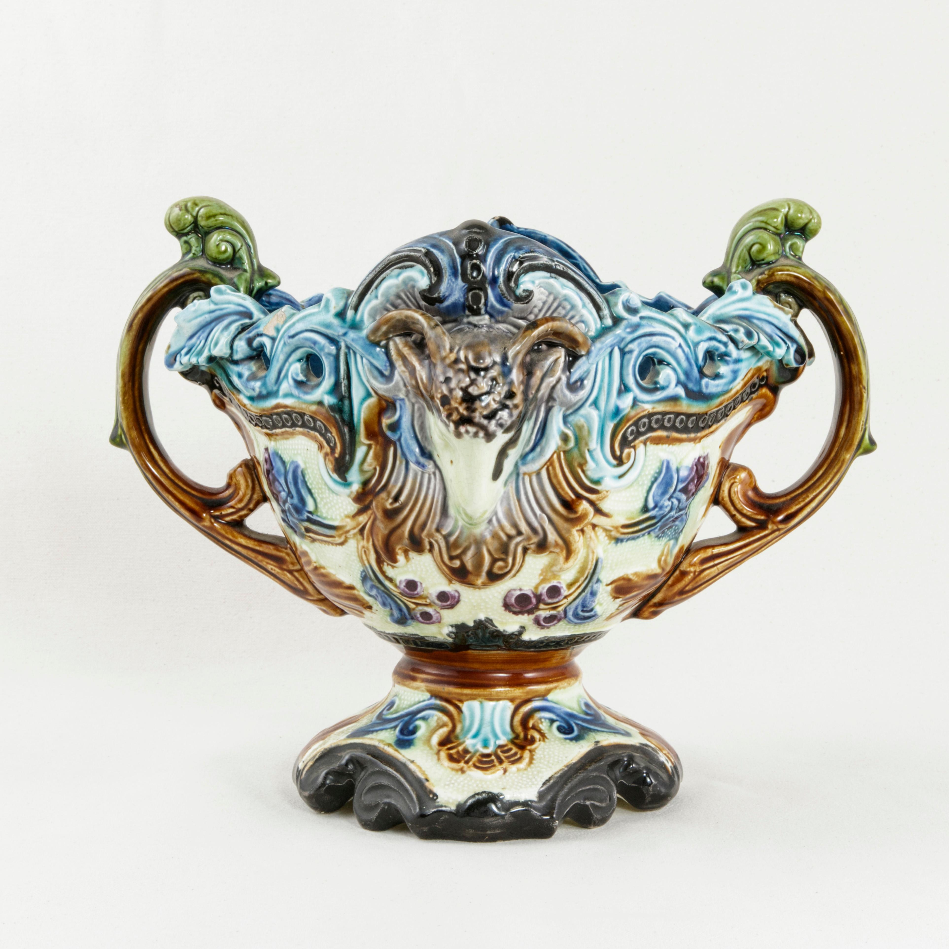 This vibrantly colored French Majolica cachepot from the late nineteenth century features rams' heads on both sides surrounded by flora and scrolling leaves. Green leaves form handles on opposing sides, circa 1880.