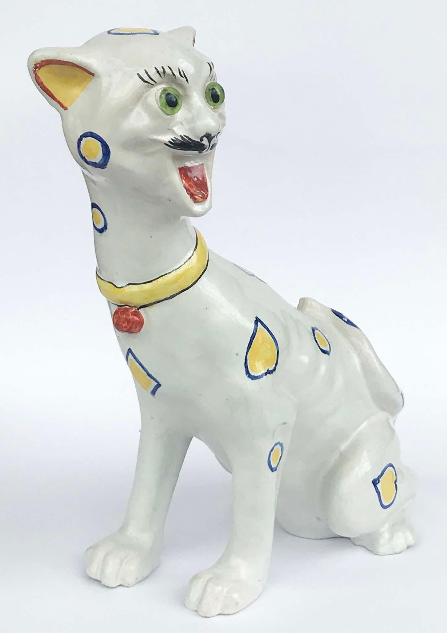 A charming late 19th century French Faience laughing cat, circa 1890 produced by the pottery manufacturer 'Mosanic', the white glazed body with hand decorated painted blue and yellow hearts, a yellow collar with deep orange bell, the head with