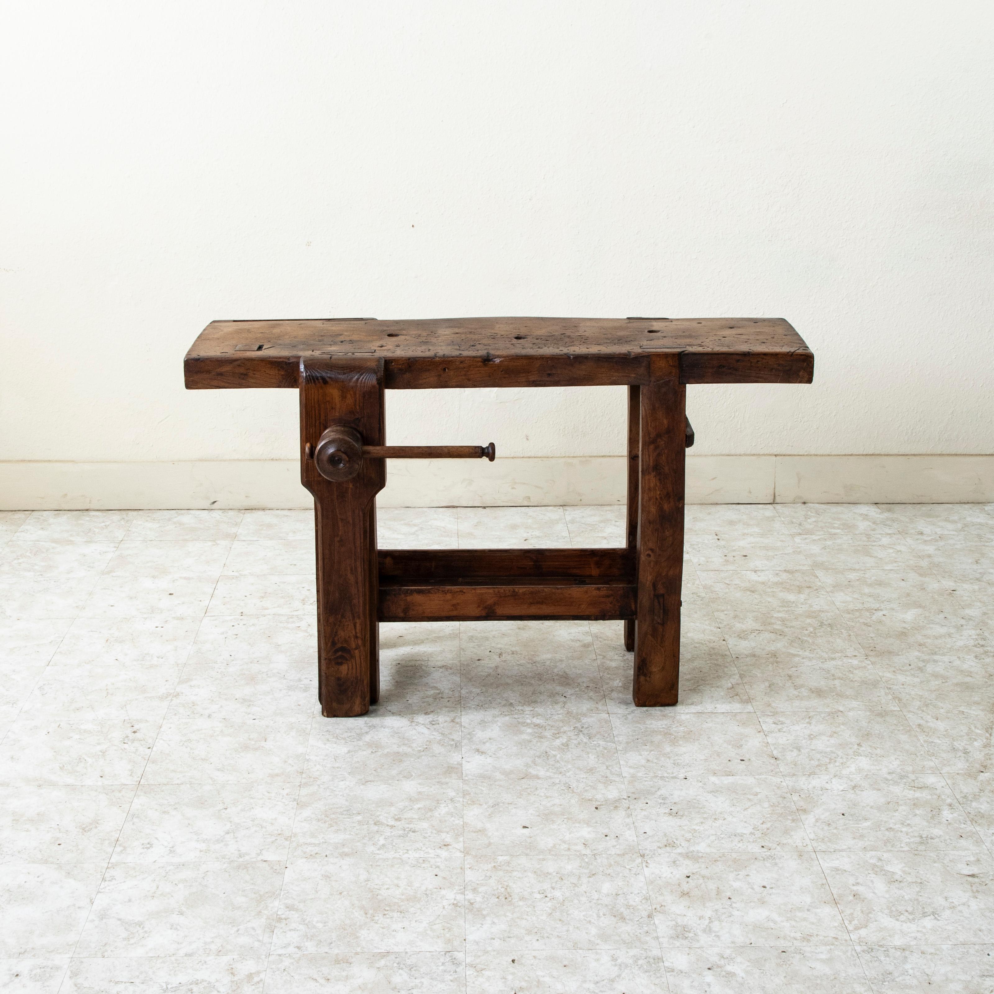 This late nineteenth century French elm workbench from the region of Normandy features a hand turned wooden screw with a wooden vise grip on the left side that can be positioned so that a bar towel can be hung from it. A slot at the back was