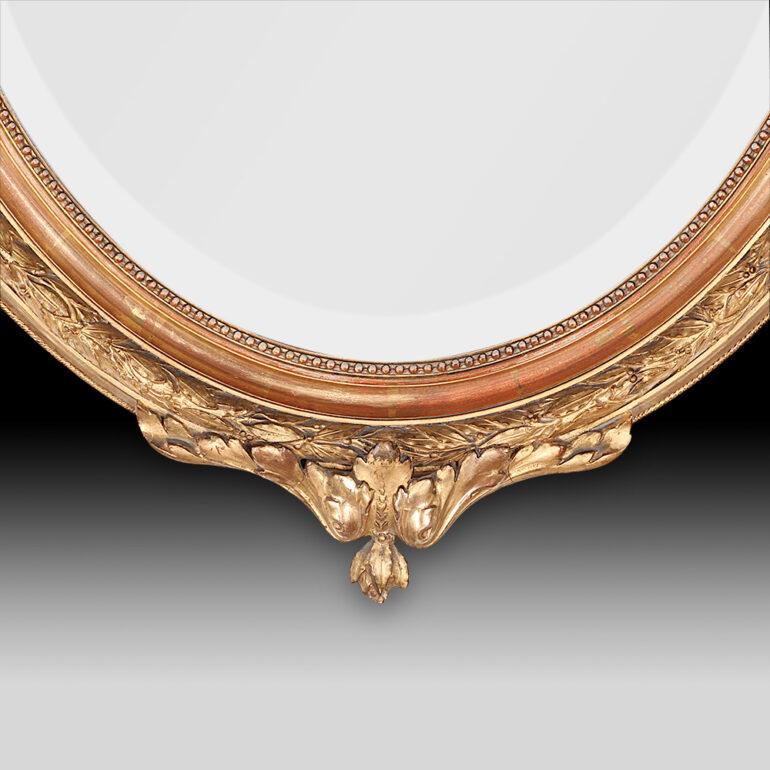 French oval gilt-framed Louis XVI style mirror with fine details and pretty carved ribbon crest. Original gold leaf finish in very good original condition with some expected 'patina' from one hundred plus years of dusting. Original beveled