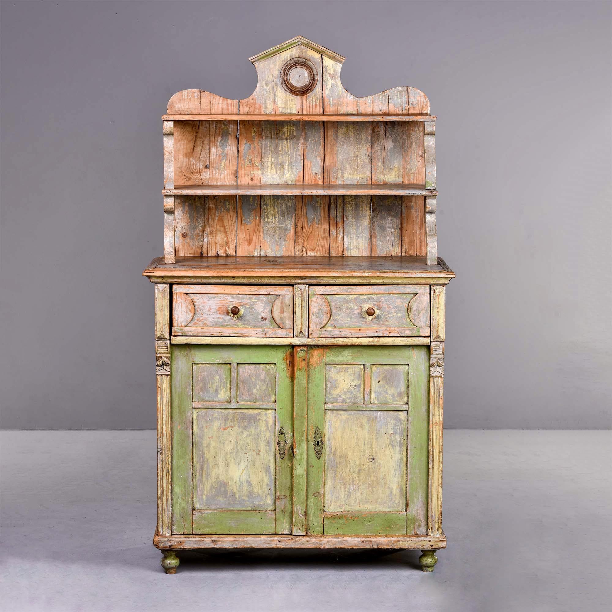 Circa 1880s French cupboard with scraped back, faded painted finish in pale green and pale blue. Top section has two open shelves and crest. Base has two drawers and storage below with single internal shelf and turned feet at front, block feet at