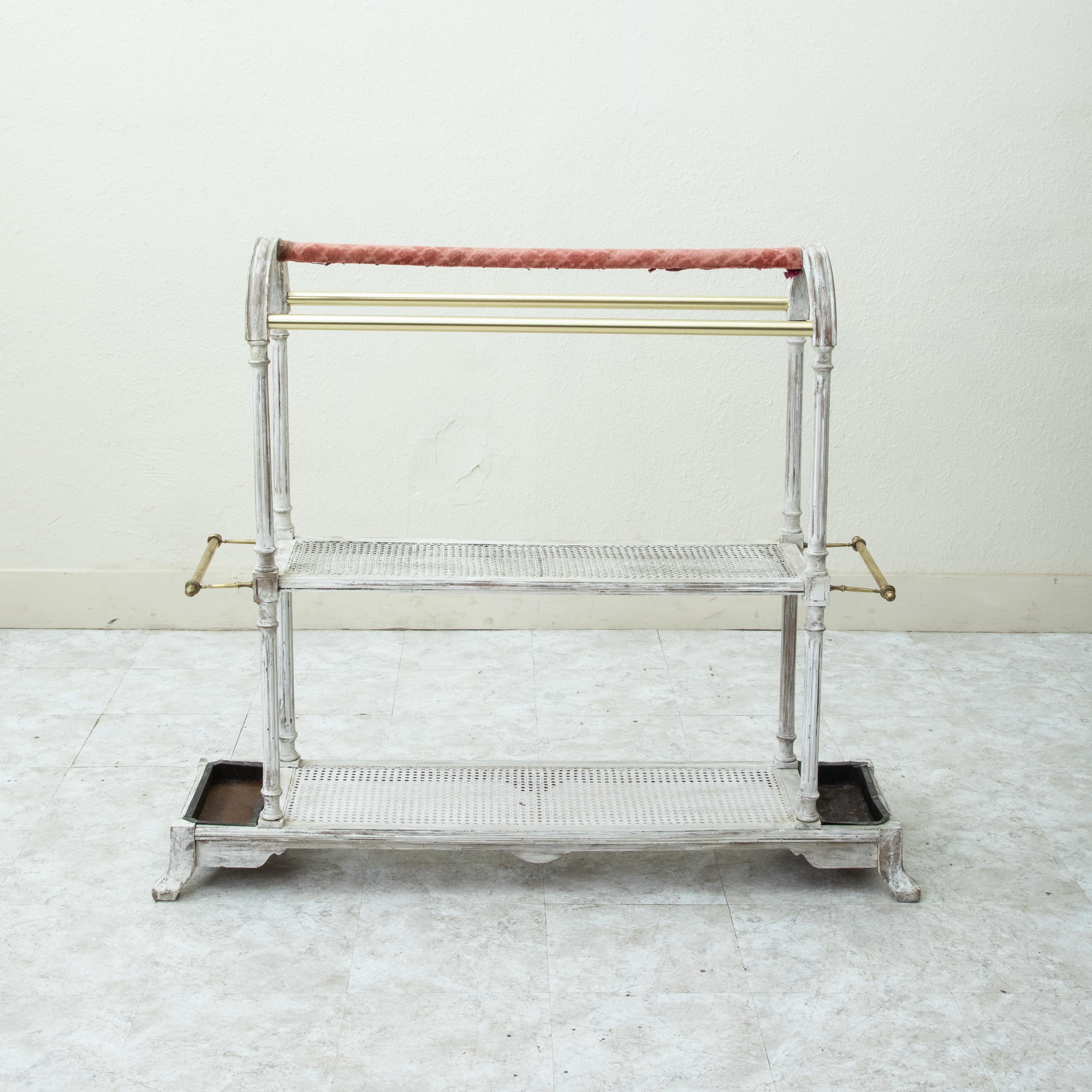 Utilisé à l'origine dans le hall d'un hôtel français pour accueillir les clients, ce support sculpté à la main est peint en blanc et présente des colonnes cannelées à chaque extrémité avec une arche au-dessus. Deux étagères cannelées permettent de