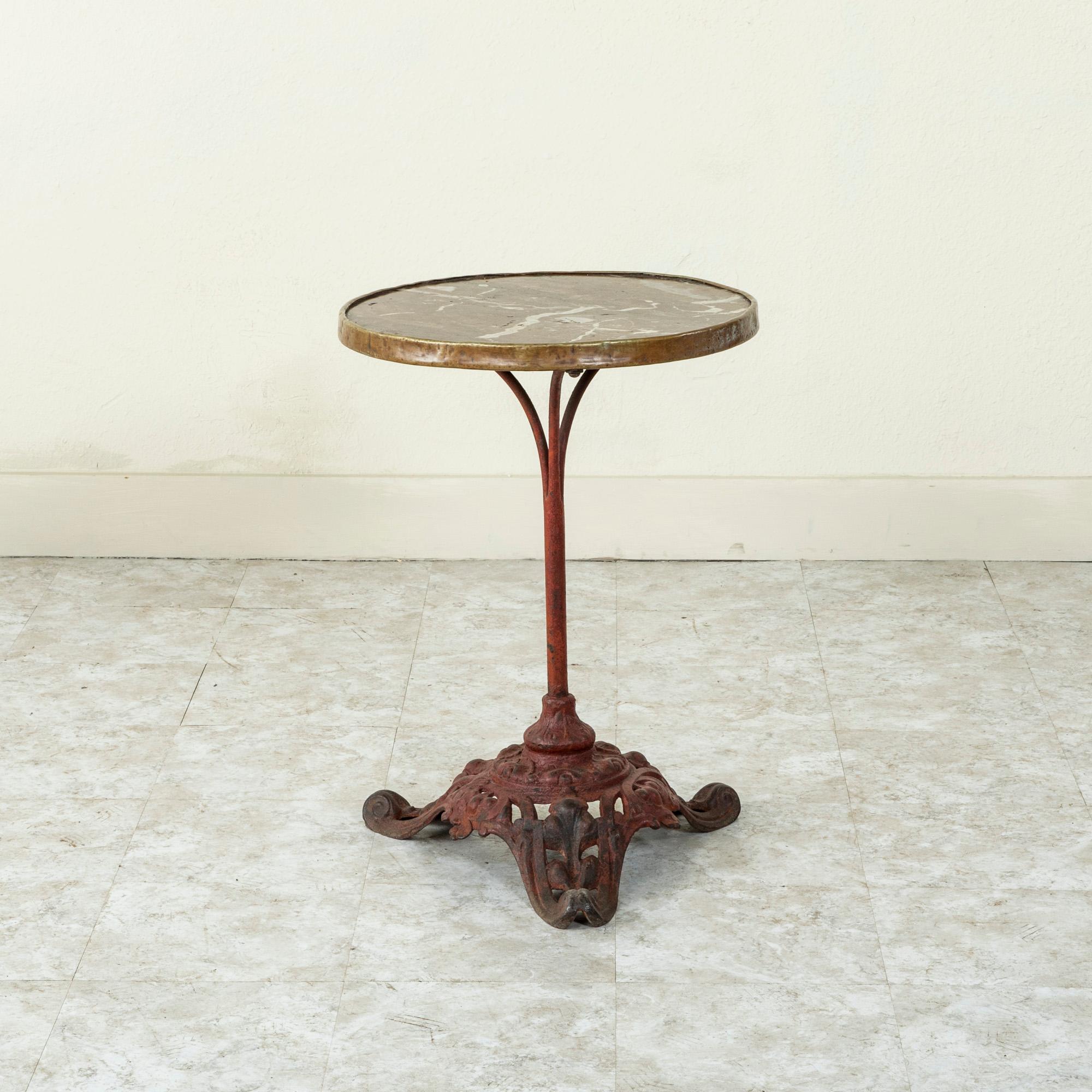 This French round bistro table from the late nineteenth century features an iron pedestal base and a deep rose colored marble top with white veining. The marble is trimmed in brass and joins the base with three arm supports. The base is painted red
