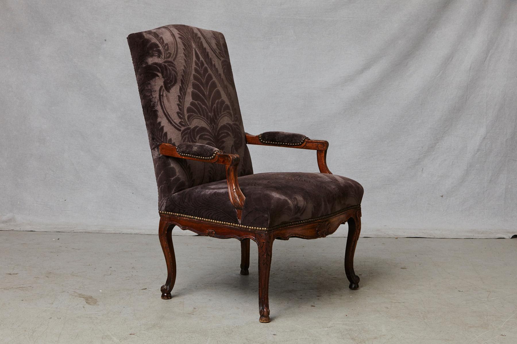 Exquisite late 19th century French Régence style walnut fauteuil or armchair with padded down scrolled arms, raised on cabriole legs with acanthus leaf carvings and escargot feet. The carved apron centred by a floral decor. Nail head trim around the